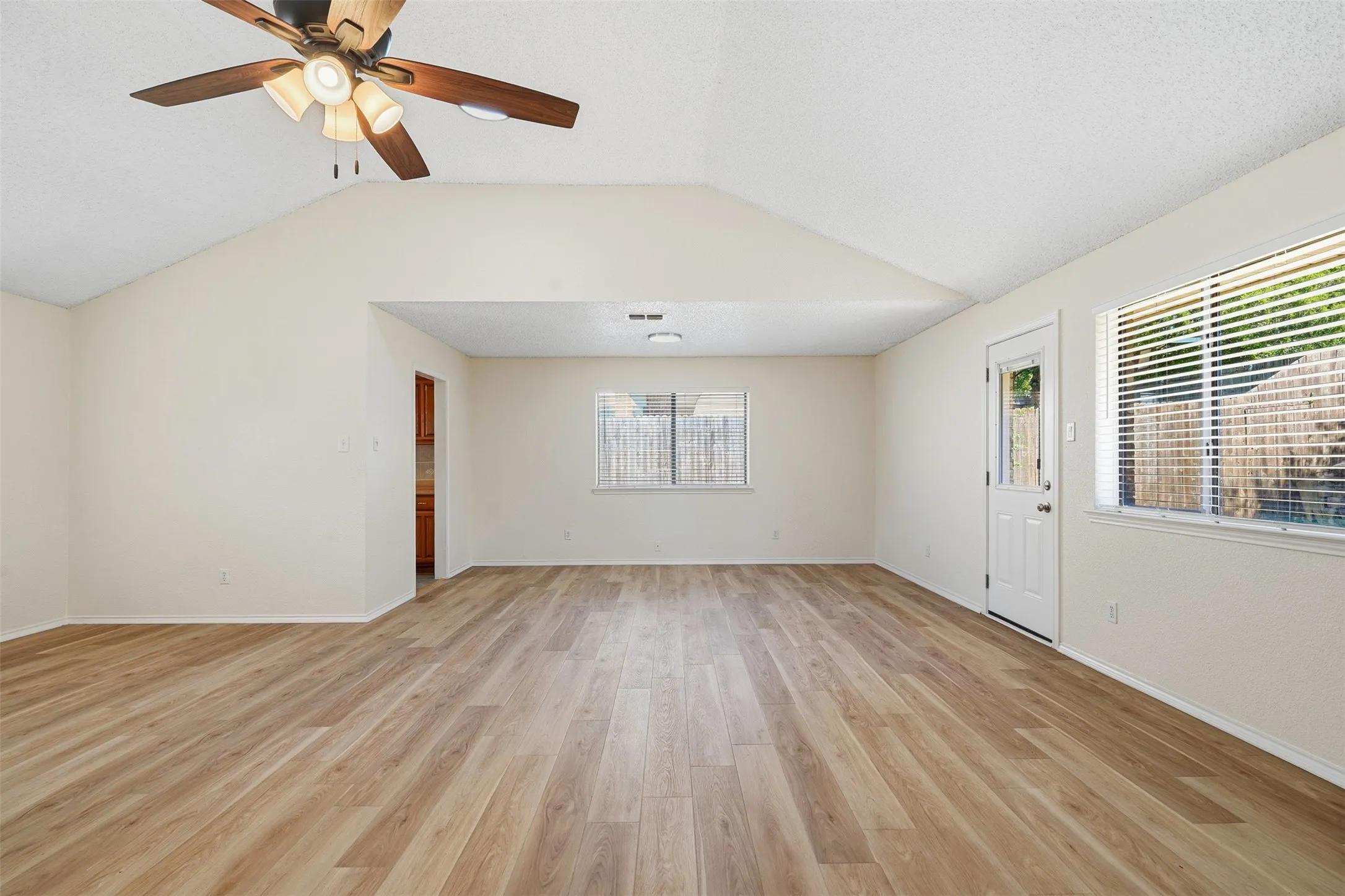 Vaulted ceilings featuring a ceiling fan, wood-finish flooring, multiple windows with blinds, and a rear exterior door