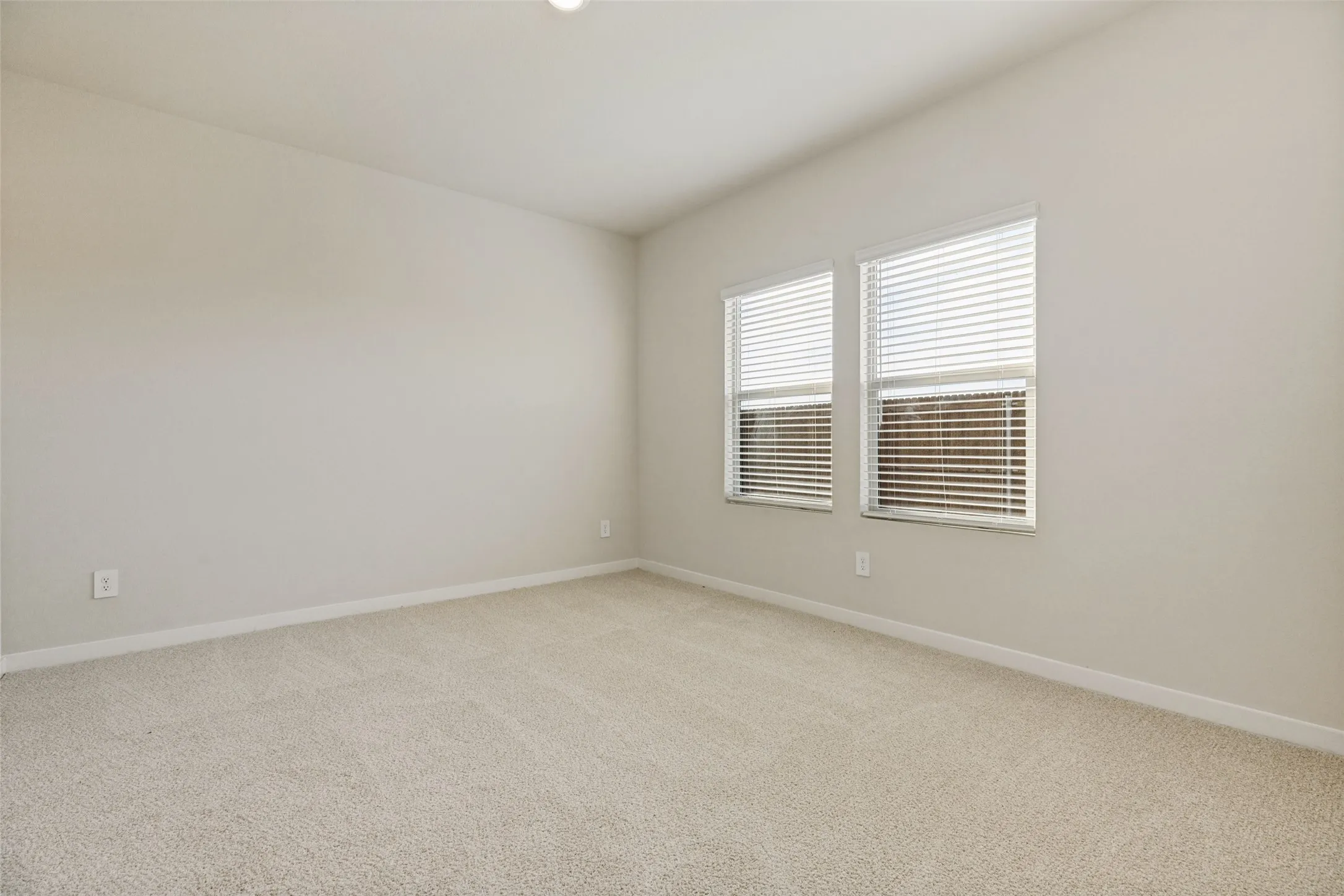 Your Own Comfortable Retreat! - The spacious primary bedroom offers plush neutral carpeting, soft natural light from two windows, and a peaceful atmosphere designed for relaxing and recharging at the end of the day.