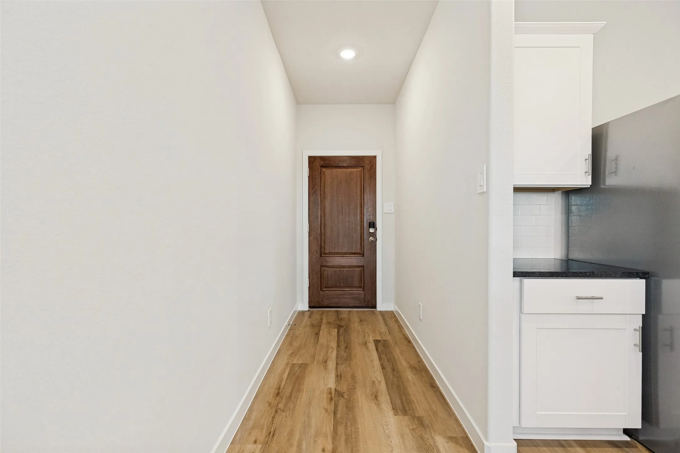 A Warm Welcome Home! - A rich stained front door opens to a bright entry hallway featuring attractive executive vinyl plank flooring, crisp white walls, and recessed lighting, setting the tone for the home's fresh, modern interior.