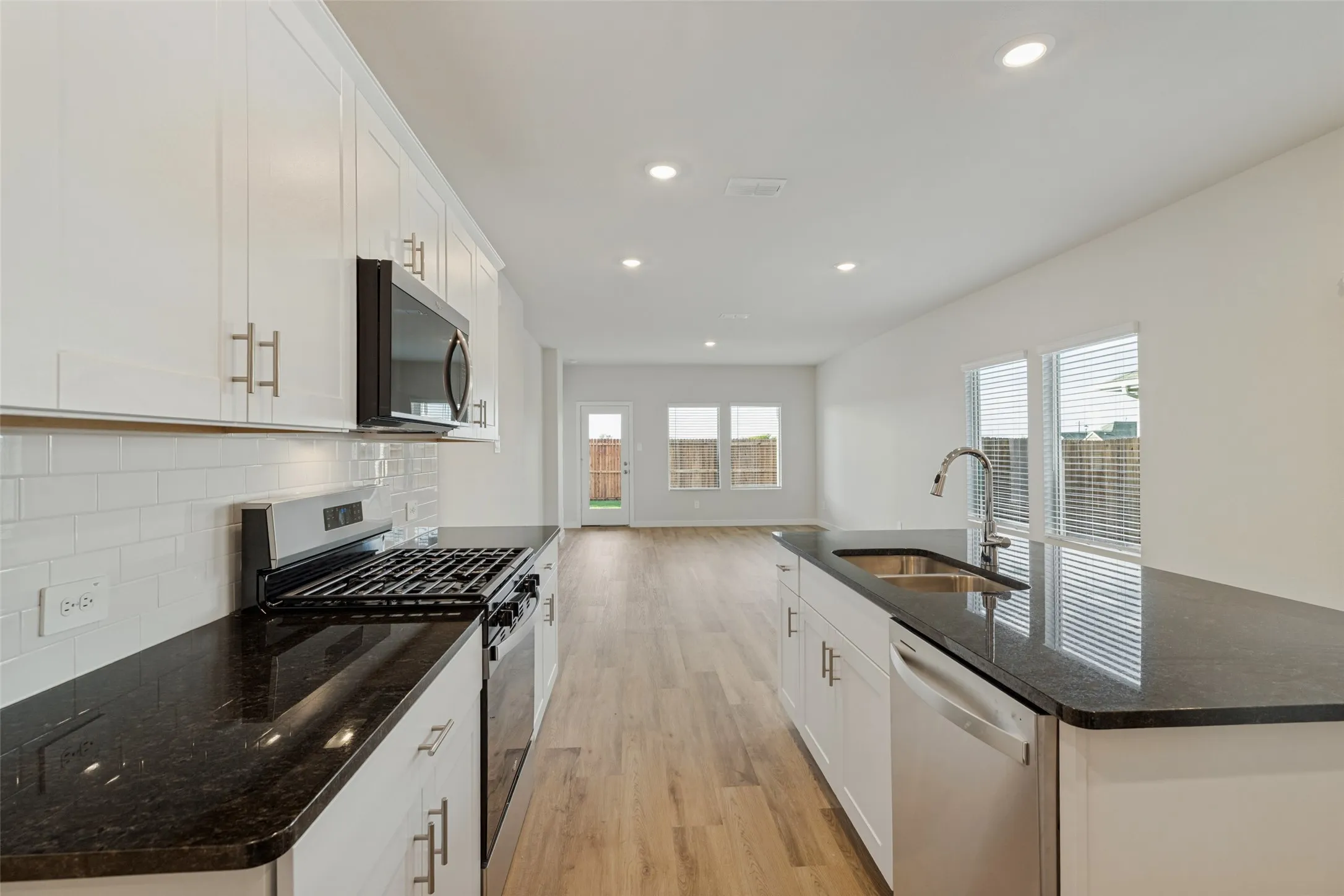 A Kitchen That Keeps Everyone Connected! - Designed for both everyday cooking and entertaining, this open kitchen features white shaker-style cabinetry, granite countertops, a classic tile backsplash, and a central island overlooking the dining and family rooms.