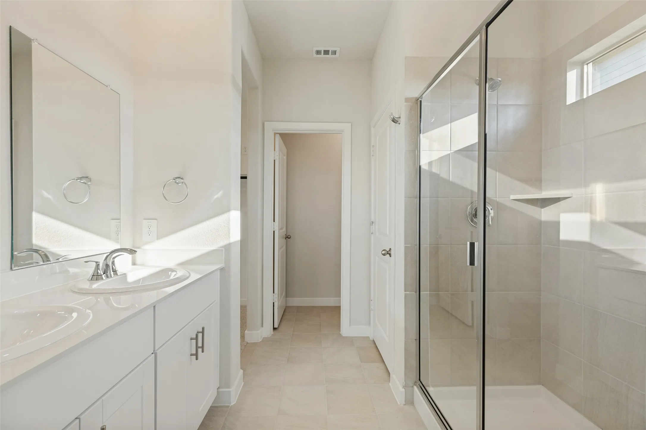 Fresh, Bright & Beautifully Functional! - The primary bathroom features a dual-sink vanity with white shaker-style cabinetry, sleek chrome fixtures, and a spacious glass-enclosed shower with ceramic tile surround. A private water closet adds everyday convenience.
