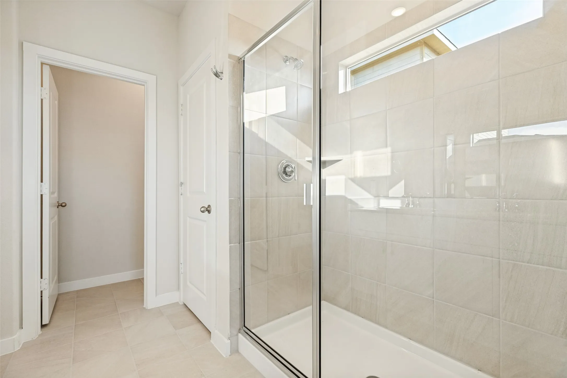 A Refreshing Start to Every Day! - The spacious walk-in shower features a ceramic tile surround, clear glass enclosure, chrome fixtures, and a high window that welcomes natural light while maintaining privacy.