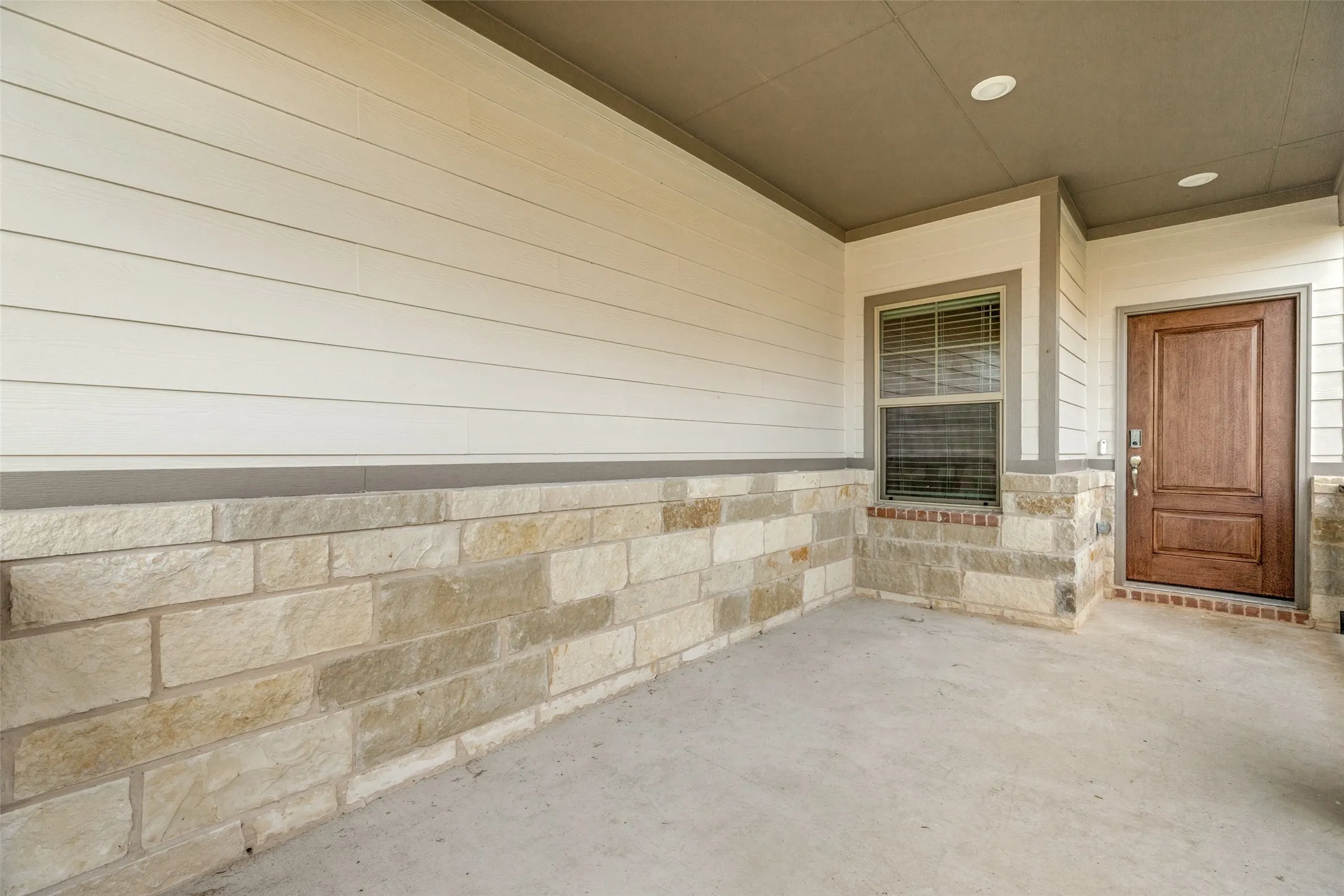 A Front Porch Made for Relaxing! - The generously sized covered porch features beautiful stone accents, low-maintenance siding, recessed lighting, and a stained front door, creating a welcoming outdoor space to enjoy morning coffee or unwind in the evening.
