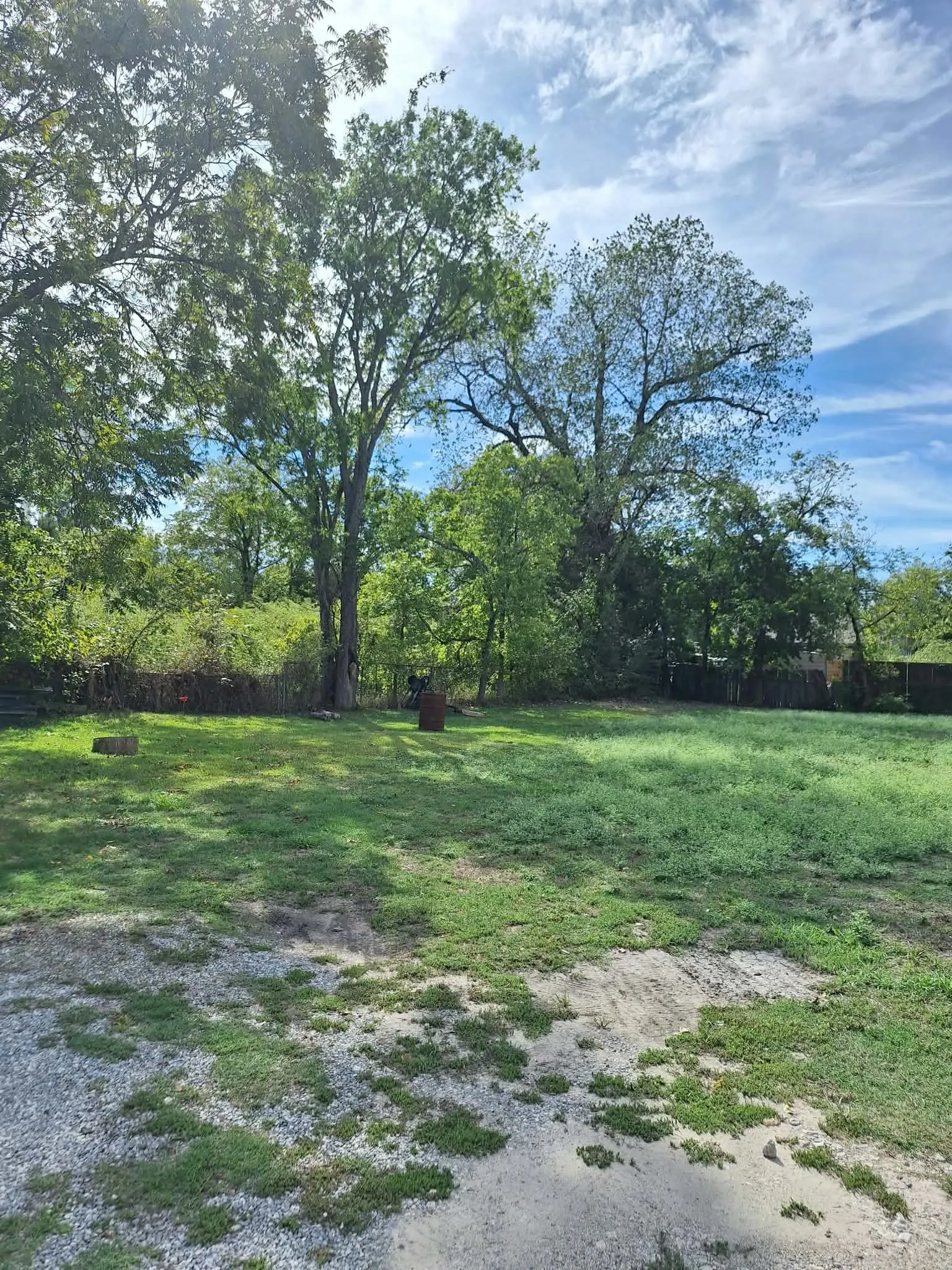 Expansive green space featuring established trees and a partially graveled area
