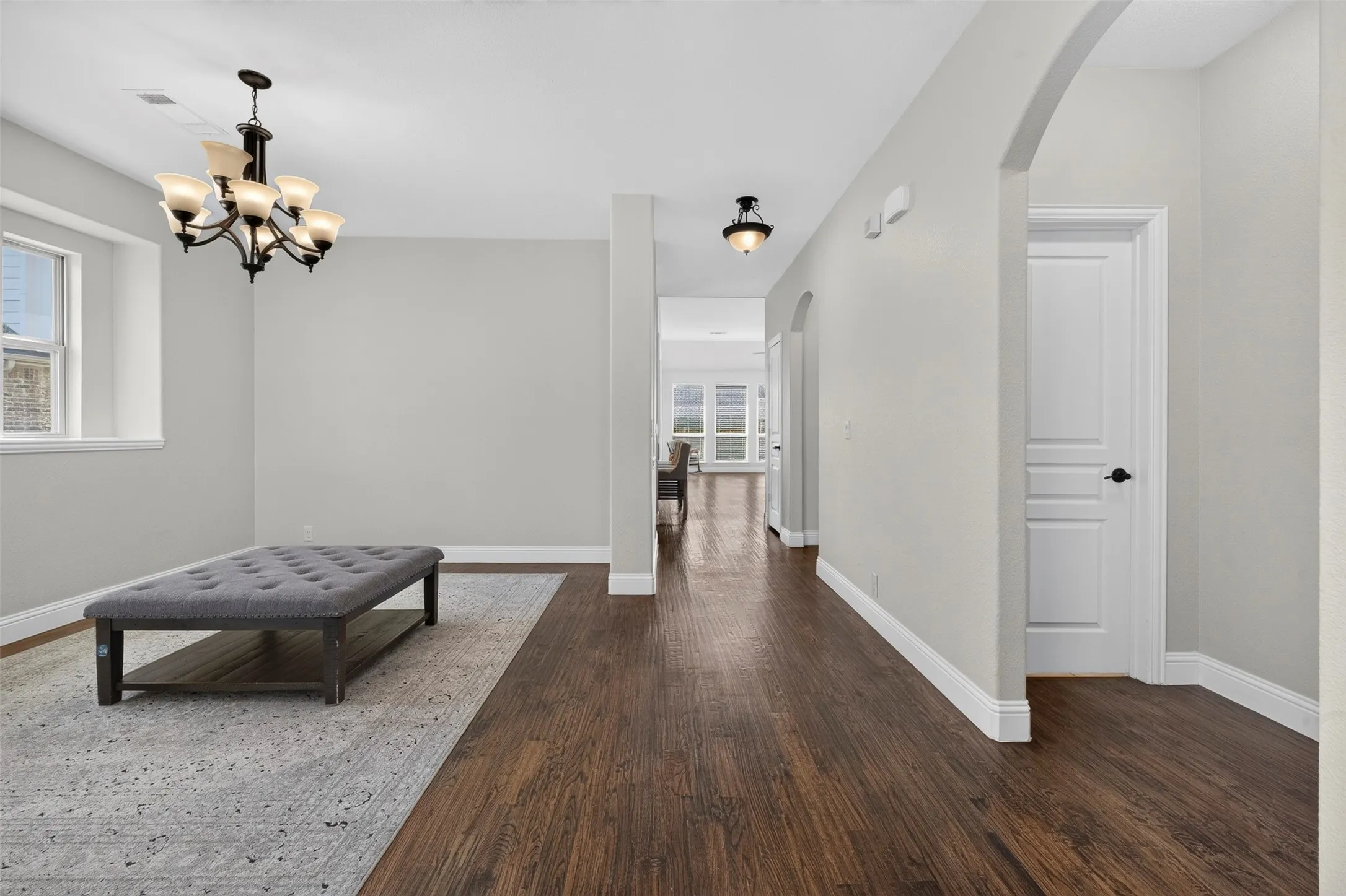 Wood-finish flooring throughout, arched entryway, white trim, and a five-light chandelier
