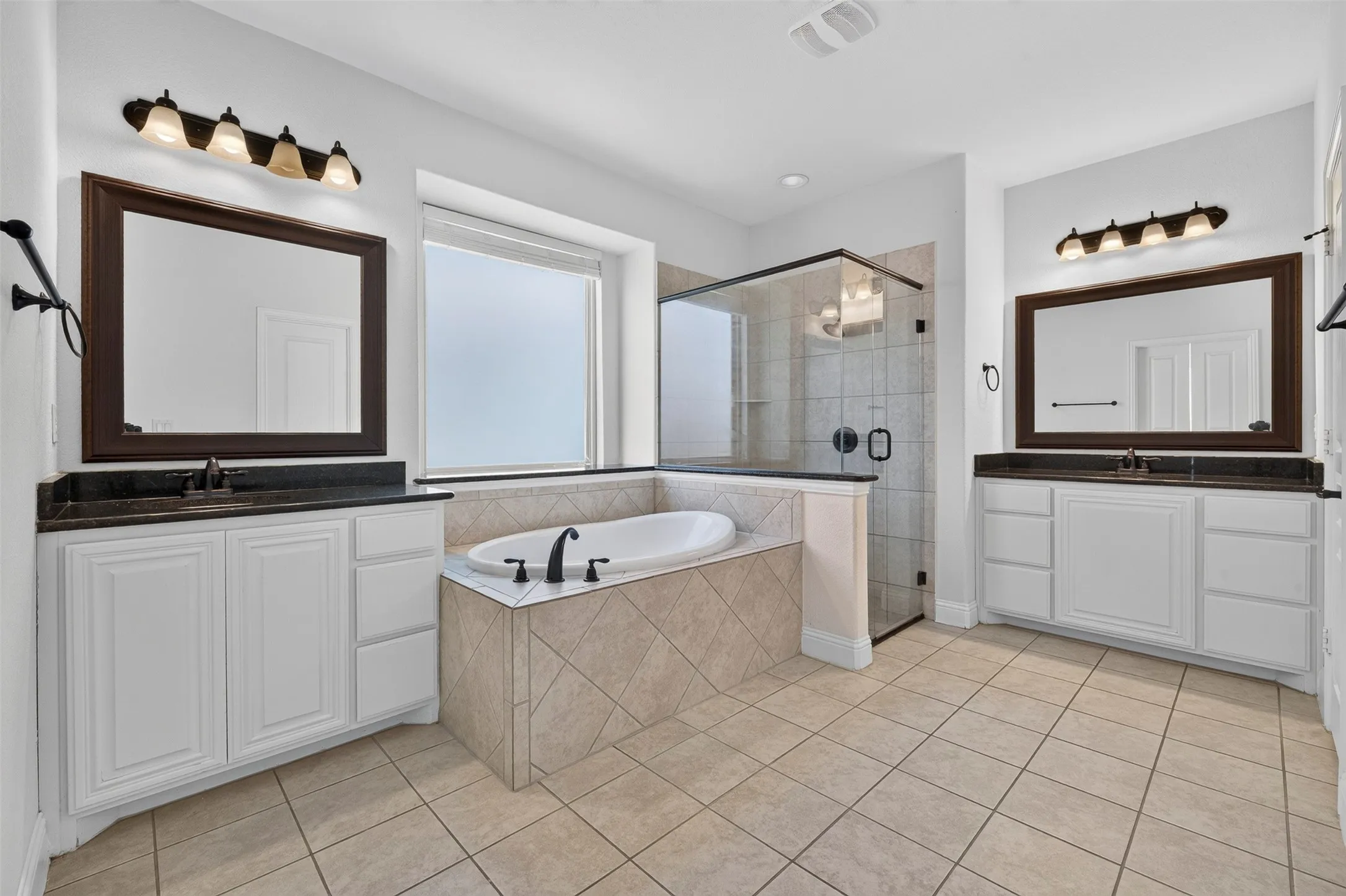Dual vanities with undermount sinks, a built-in soaking tub, a separate glass-enclosed shower, and tile flooring