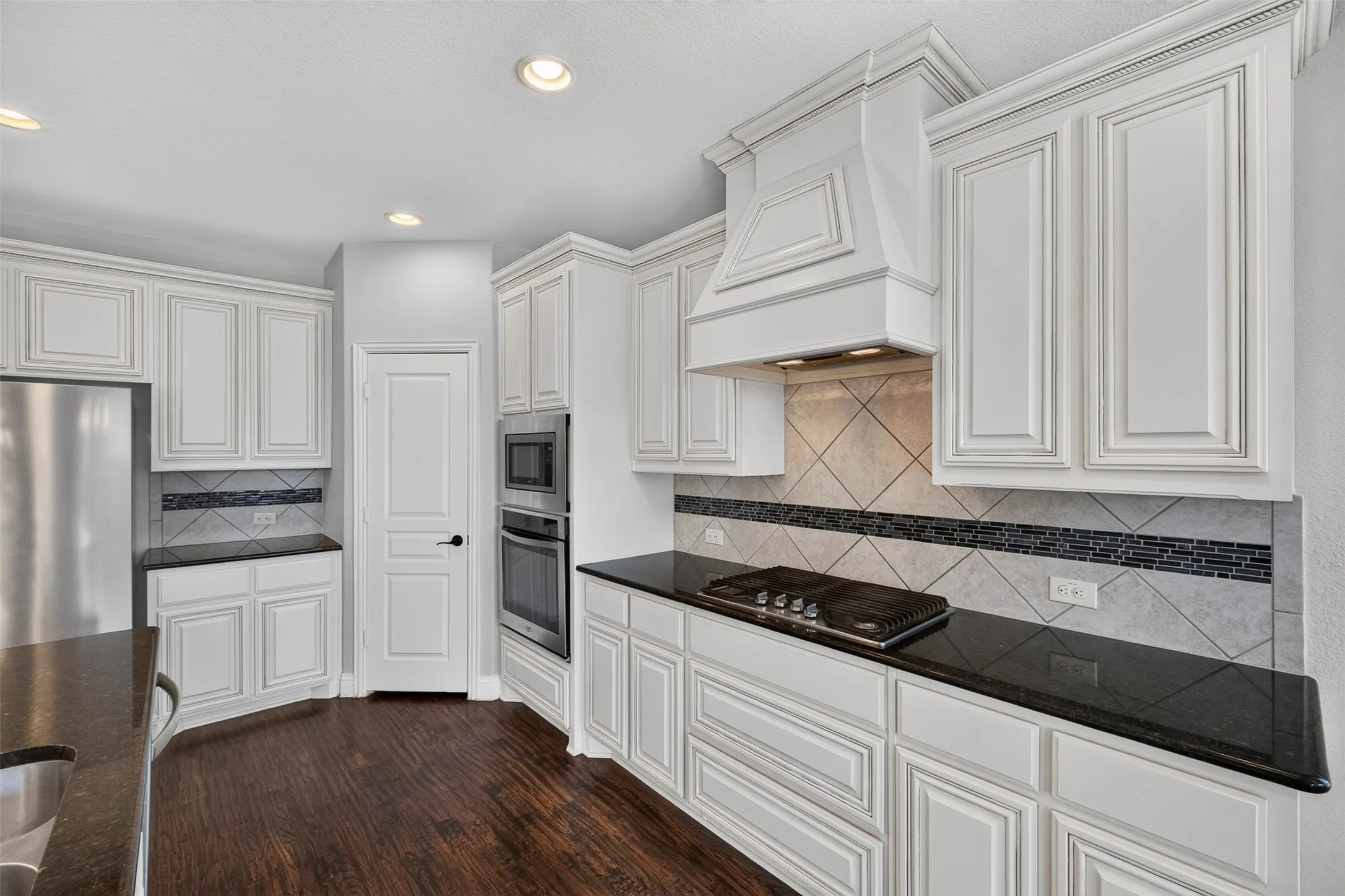 Kitchen featuring white cabinetry, dark countertops, wood-finish flooring, a tile backsplash, and stainless steel built-in appliances