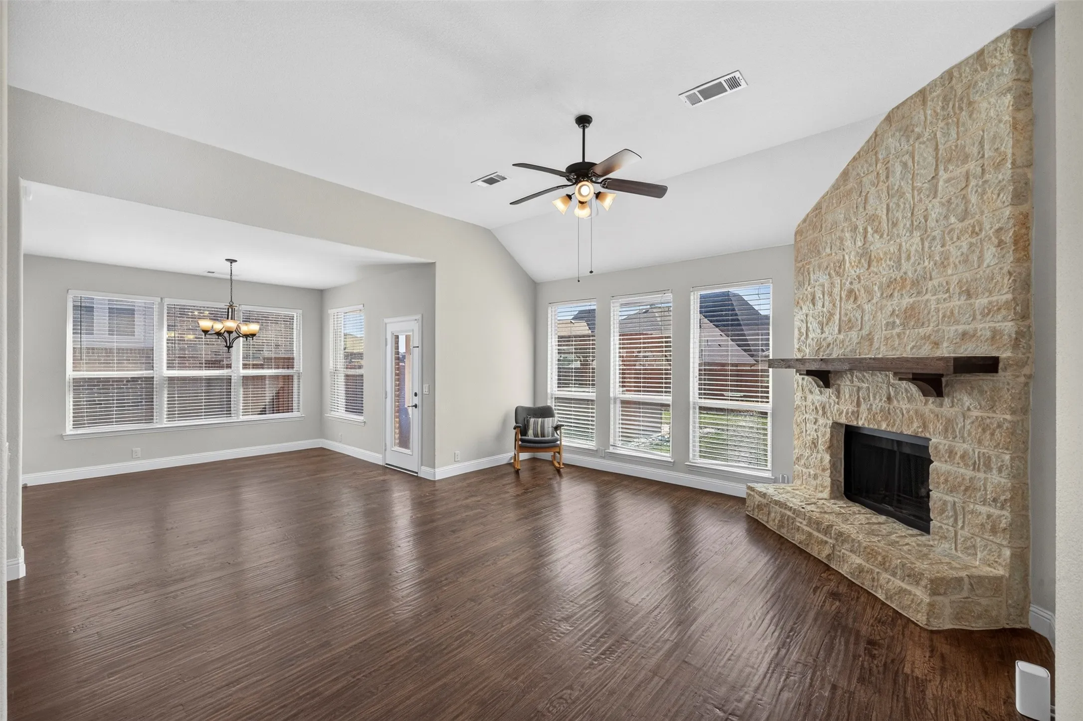 Vaulted ceilings, wood-finish flooring, stone fireplace with a wood mantle, numerous windows, and a ceiling fan with integrated lighting