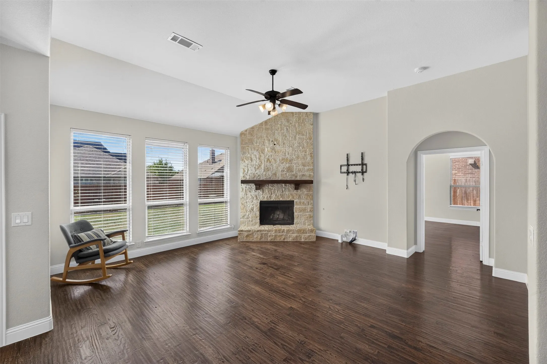 Vaulted ceiling, dark wood-finish flooring, stone-clad fireplace with wood mantel, ceiling fan, and arched doorway