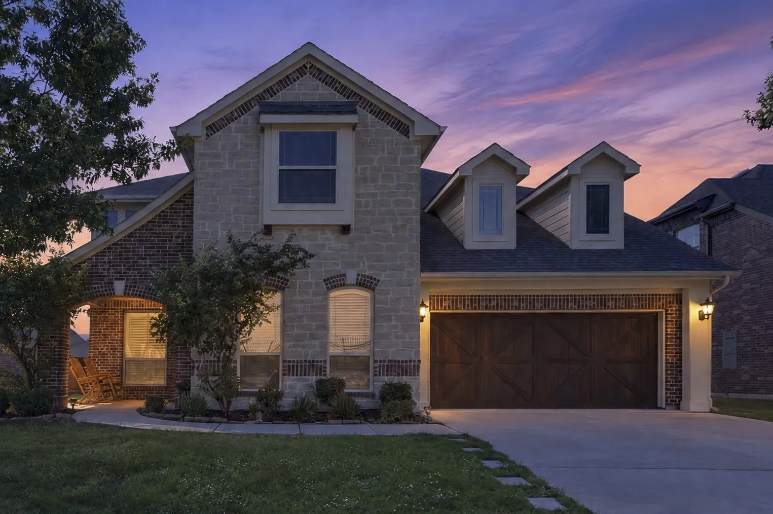 Stone and brick exterior with multiple gabled rooflines and dormer windows, illuminated by exterior sconces