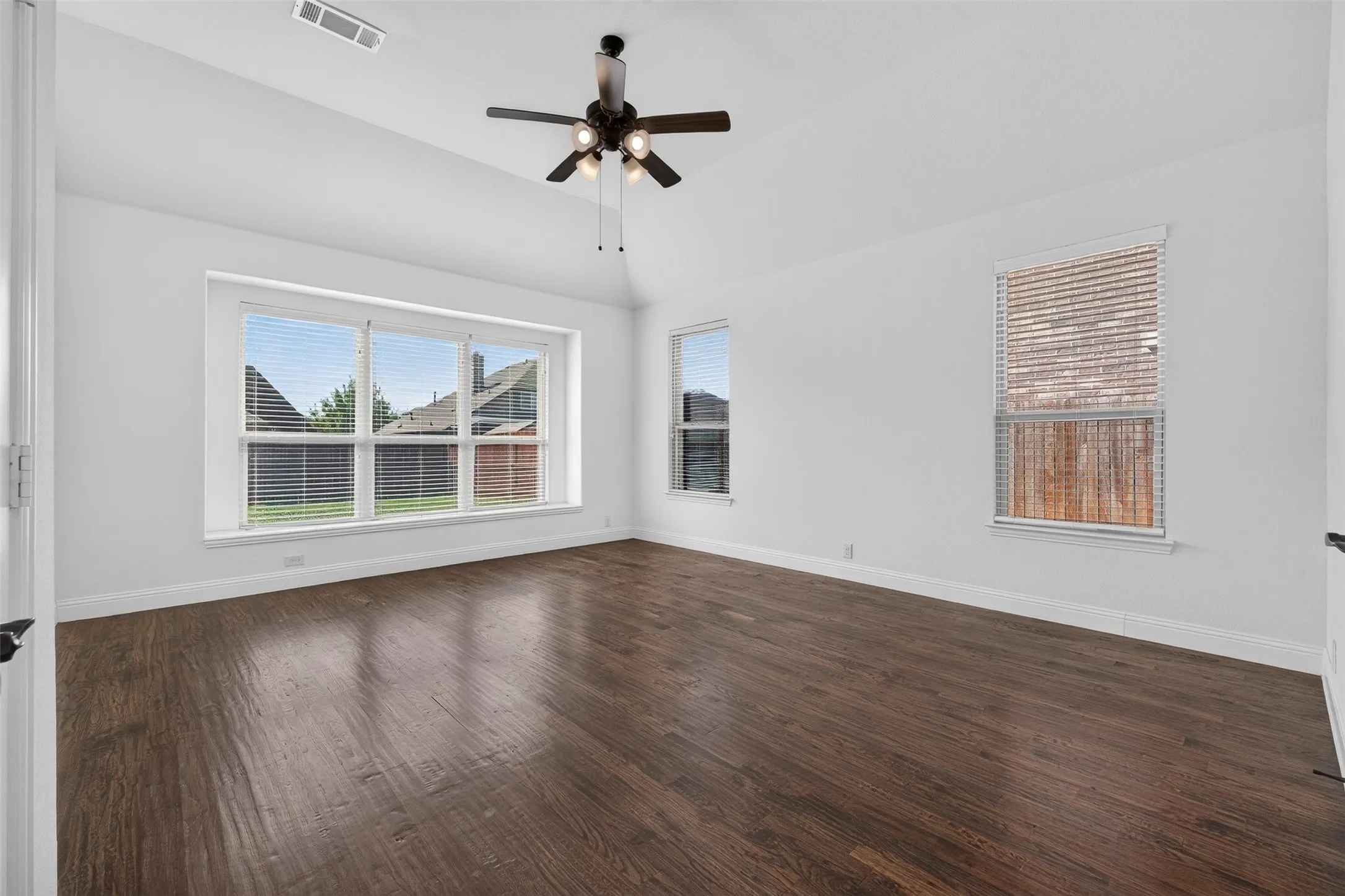 Vaulted ceiling with a ceiling fan, wood-finish flooring, and multiple windows
