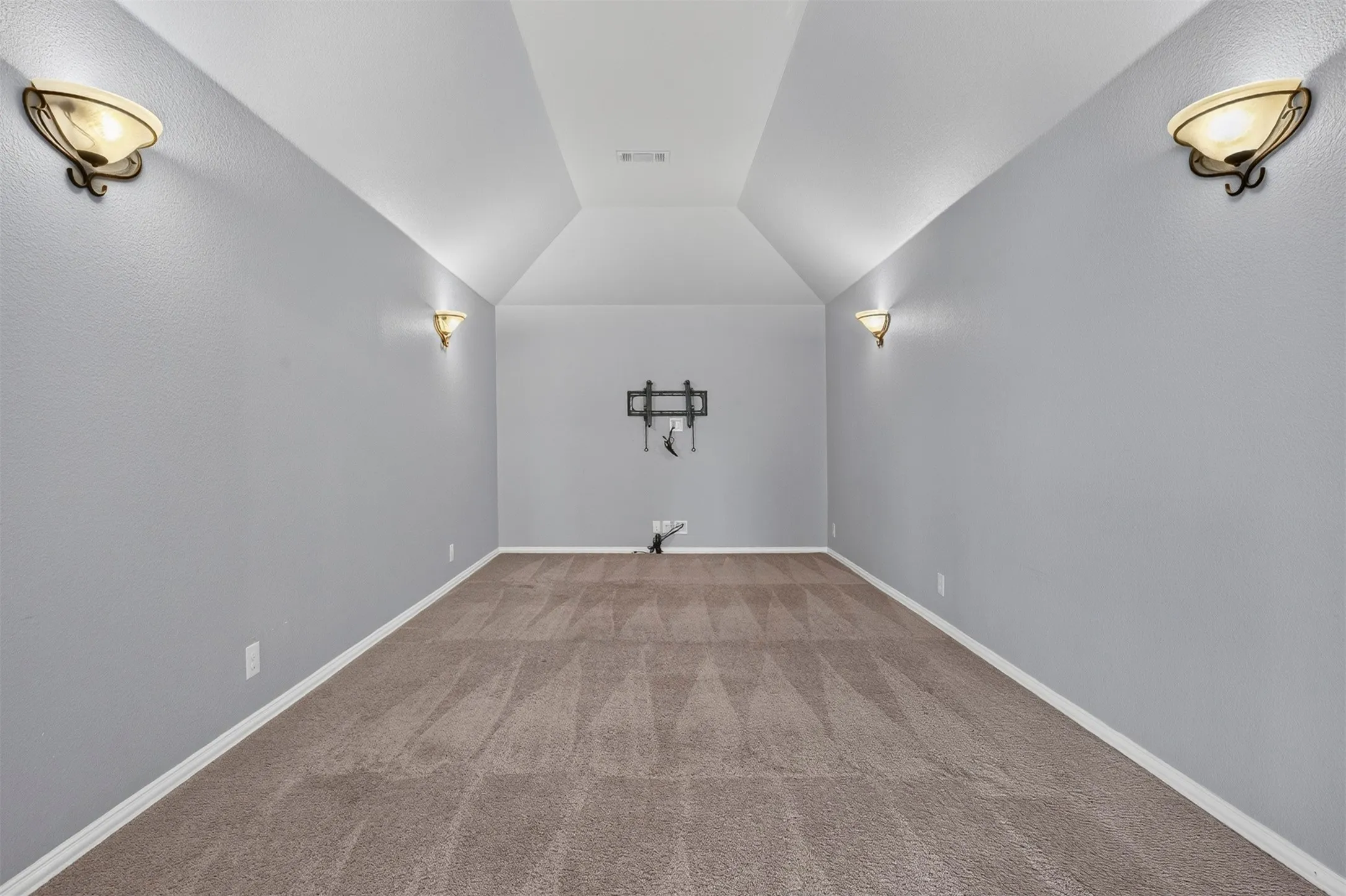 Vaulted ceiling with a central mounted lighting fixture, textured walls, and wall sconces