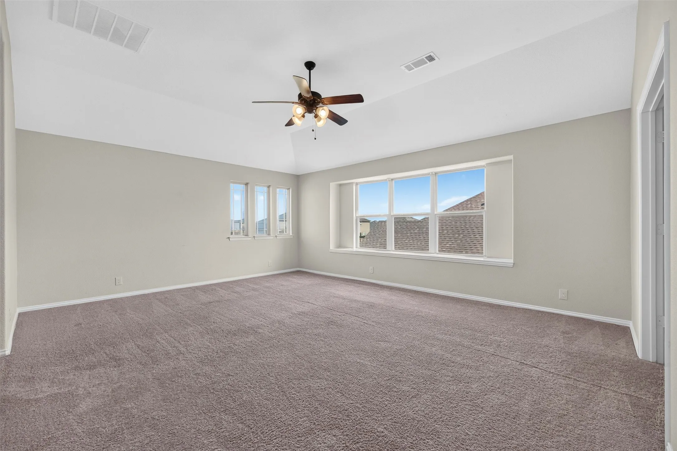 Spacious room featuring vaulted ceilings, a ceiling fan, multiple windows, and neutral carpeting