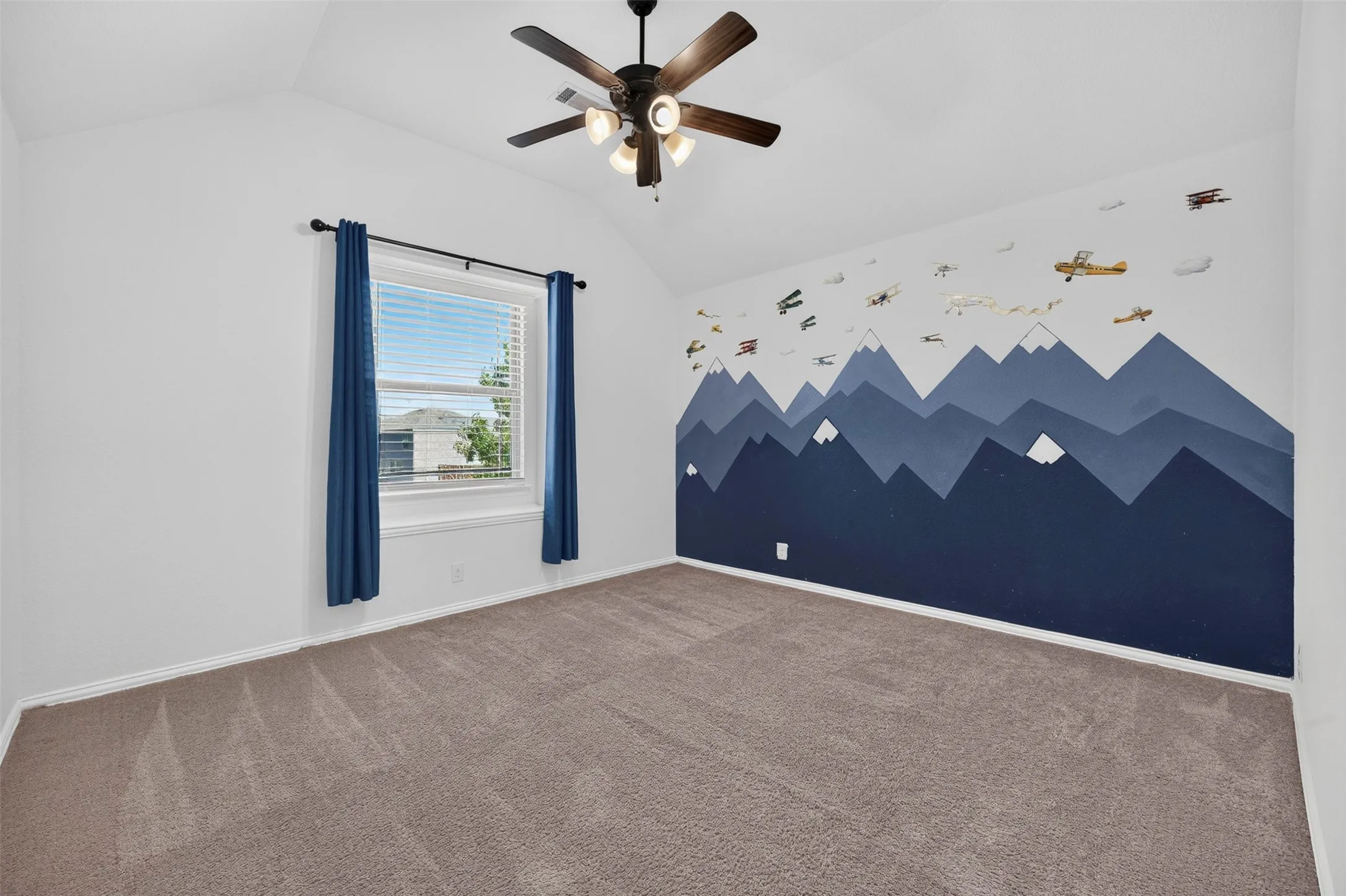 Bright bedroom featuring neutral carpet flooring, a ceiling fan with integrated lighting, and a striking navy mountain mural accent wall