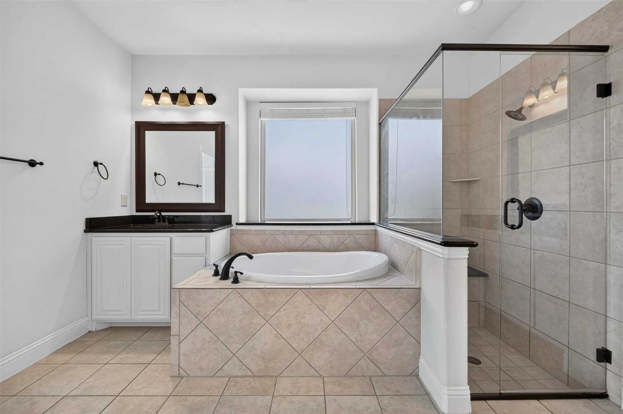 Spacious bathroom featuring a built-in soaking tub, a separate glass-enclosed shower, a vanity with dark countertop, and tiled flooring