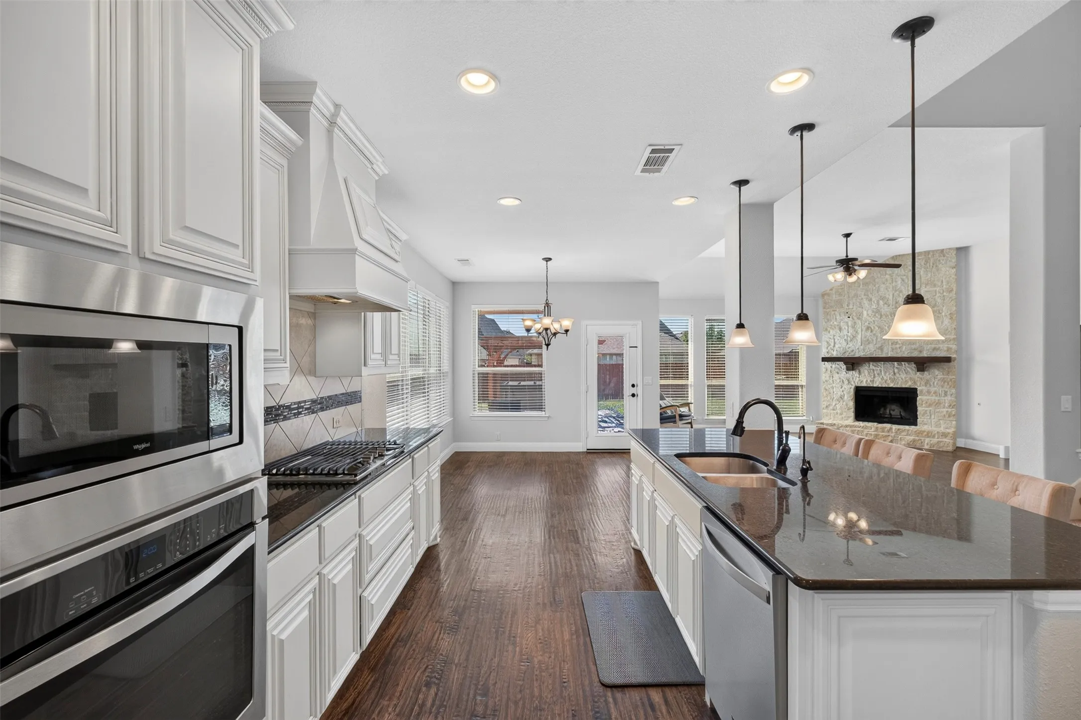 Kitchen featuring white cabinetry, dark countertops, built-in stainless steel appliances, a large island with sink, and wood-finish flooring