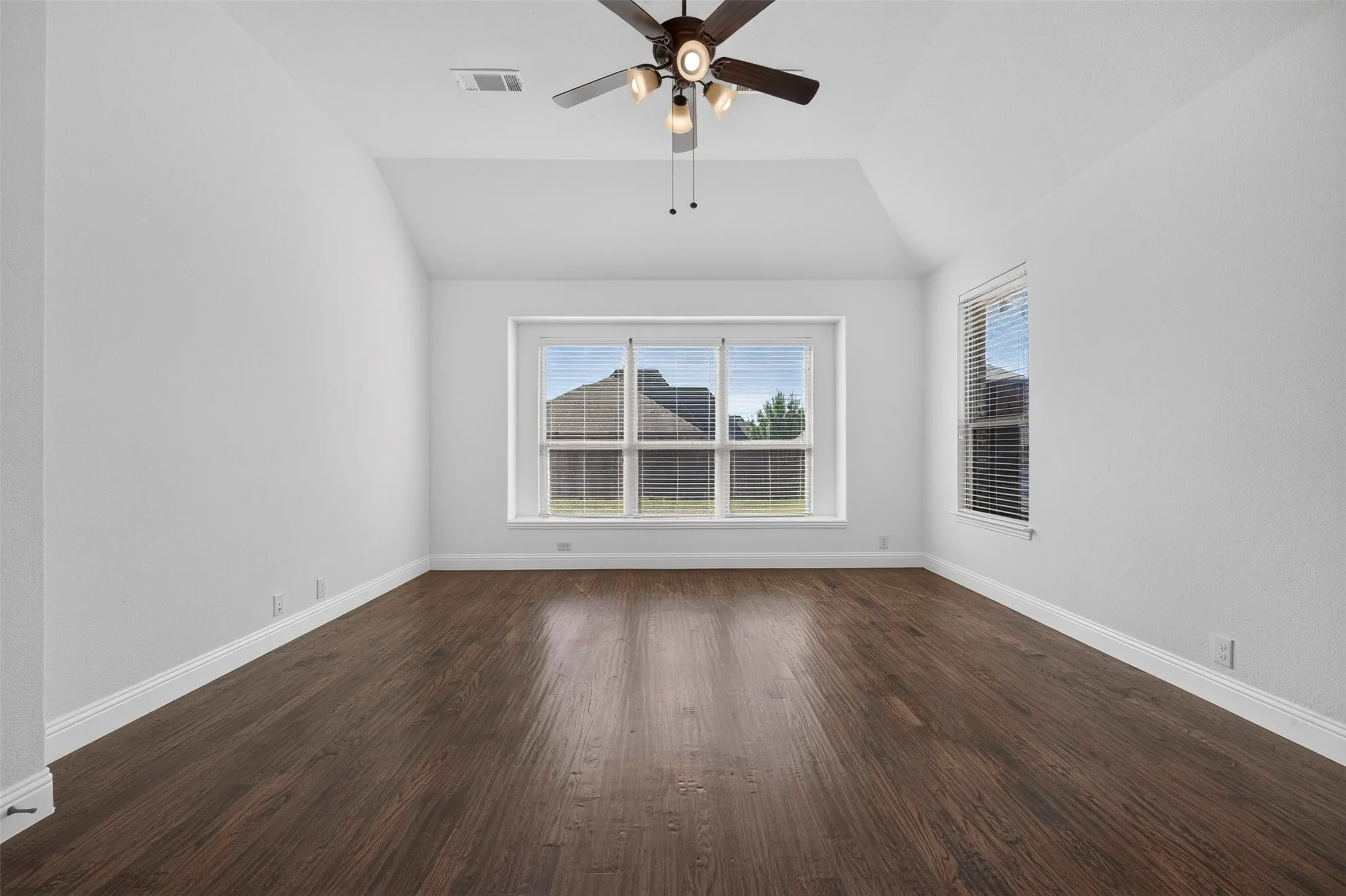 Vaulted ceiling, ceiling fan with integrated lighting, wood-finish flooring, multiple windows, and white walls
