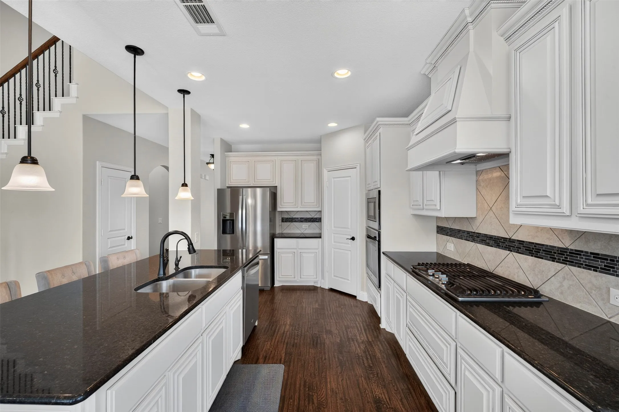 Kitchen featuring dark wood-finish flooring, white cabinetry, dark countertops, a stainless steel refrigerator, and a gas cooktop with a custom range hood