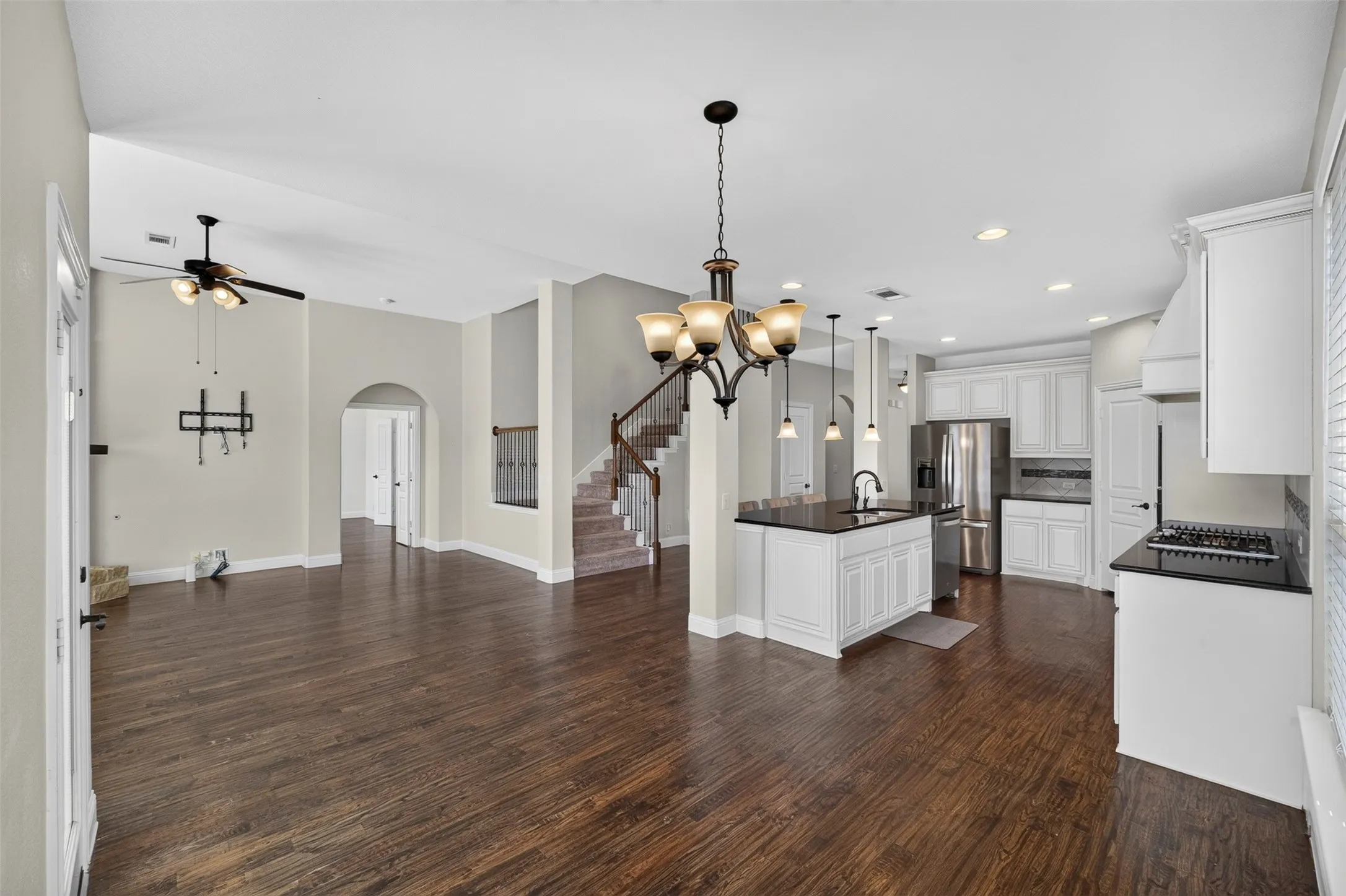 Open-concept living space showcasing rich wood-finish flooring, white cabinetry with a large center island featuring dark countertops, stainless steel appliances, and pendant lighting