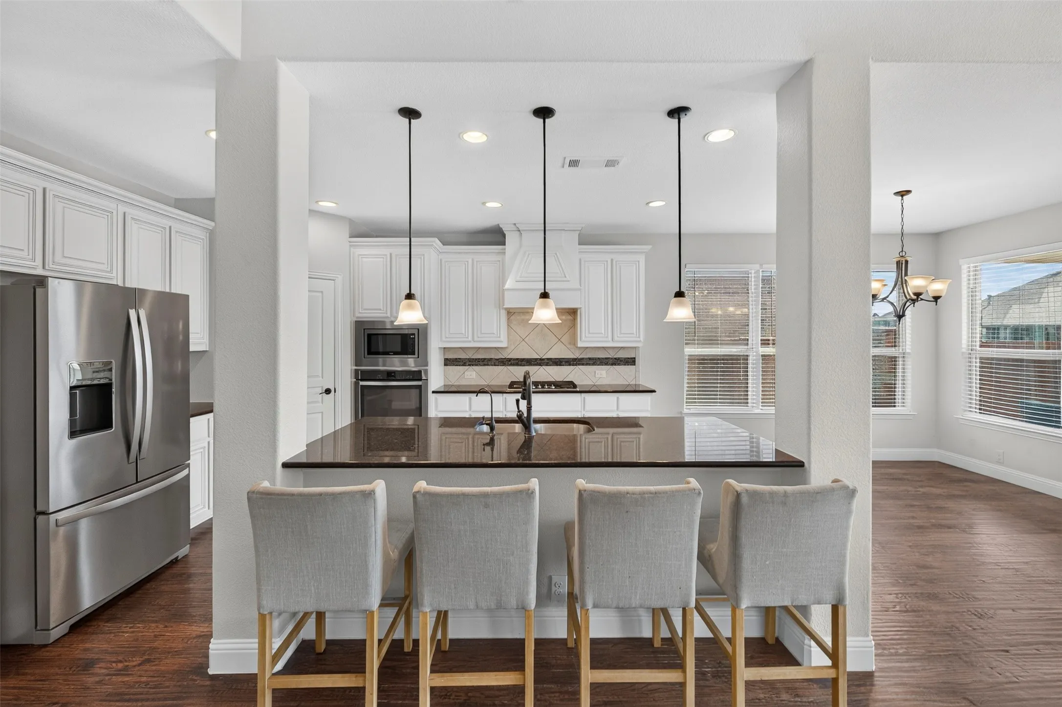 Open-concept kitchen and dining area featuring a large center island with wood-finish countertops, stainless steel appliances including a French-door refrigerator, pendant lighting, white cabinetry, and wood-finish flooring throughout
