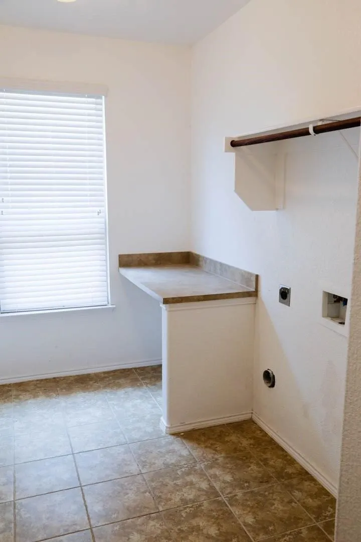 Tile flooring, built-in countertop, window with blinds, overhead light fixture, clothing rod with shelving