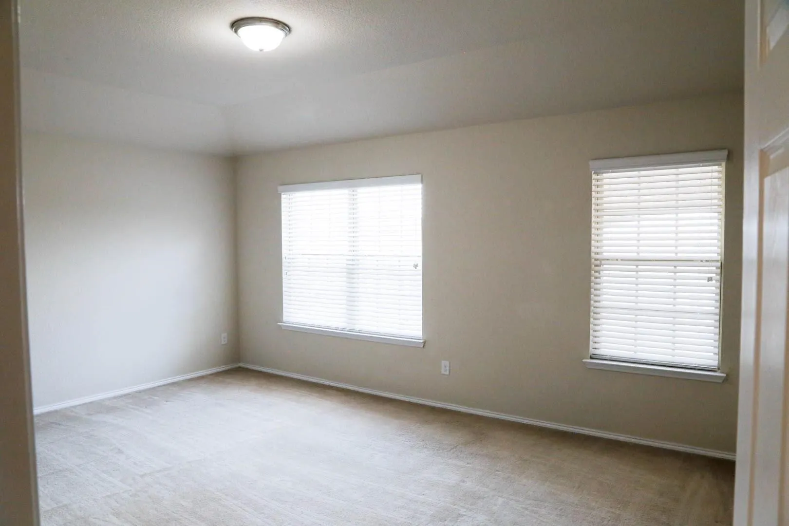 Recessed ceiling with flush mount lighting, two windows with blinds, and light-toned flooring