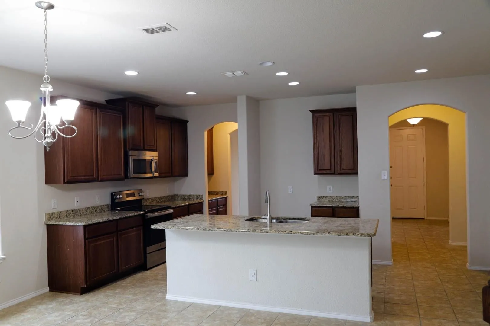 Kitchen featuring dark wood-finish cabinetry, granite countertops, tile flooring, stainless steel appliances, and recessed lighting