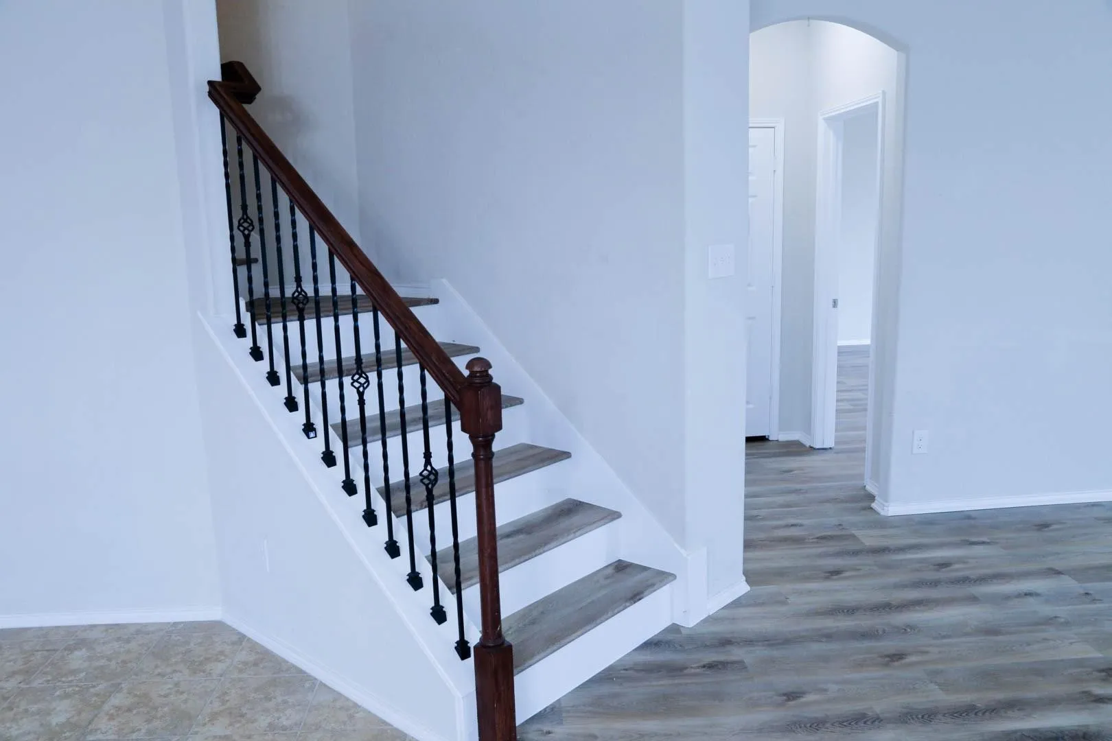 Staircase with wood-finish treads, dark wood-finish handrail, and wrought iron balusters
