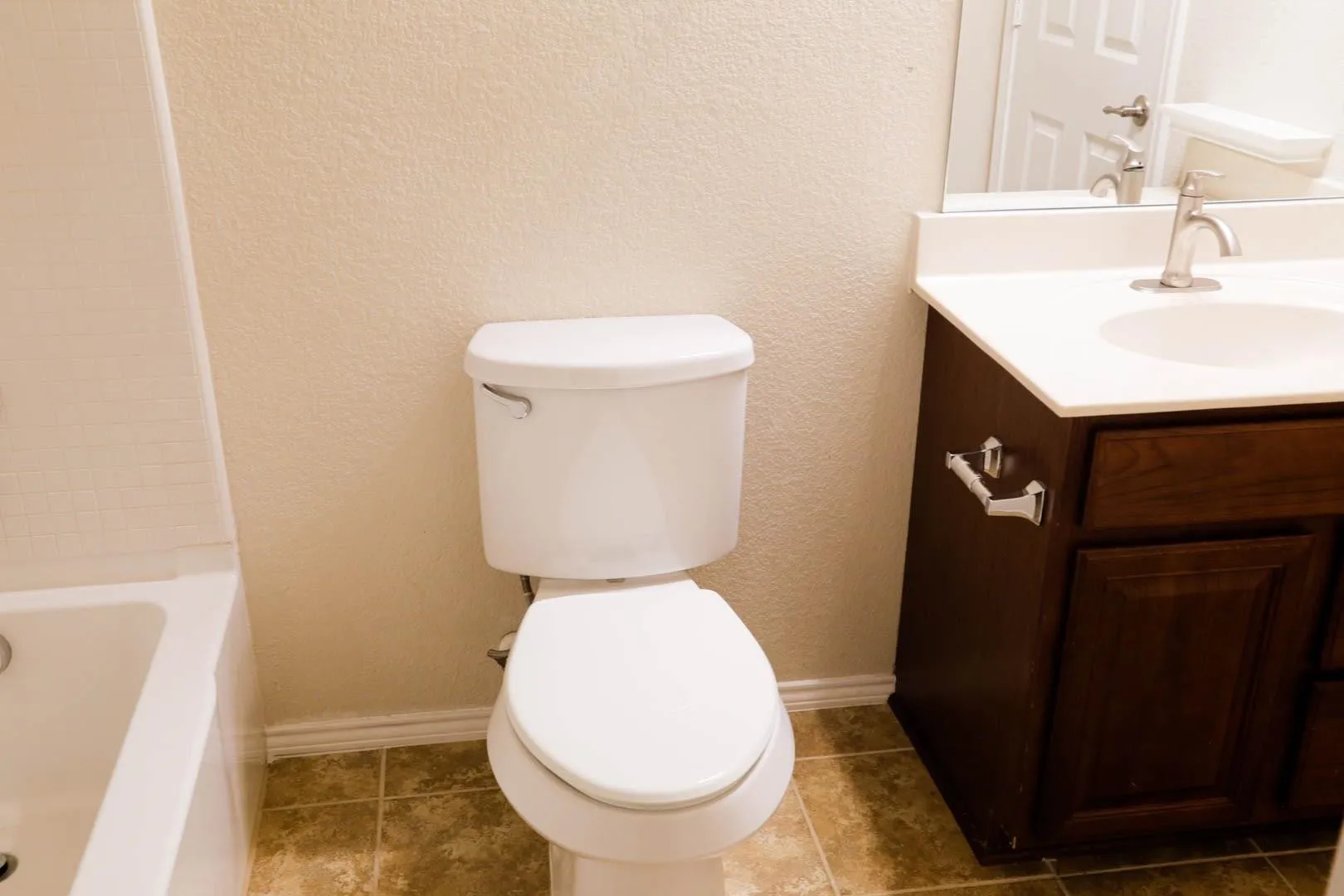 White porcelain toilet, dark wood-finish vanity with white countertop, integrated sink, and brushed nickel faucet
