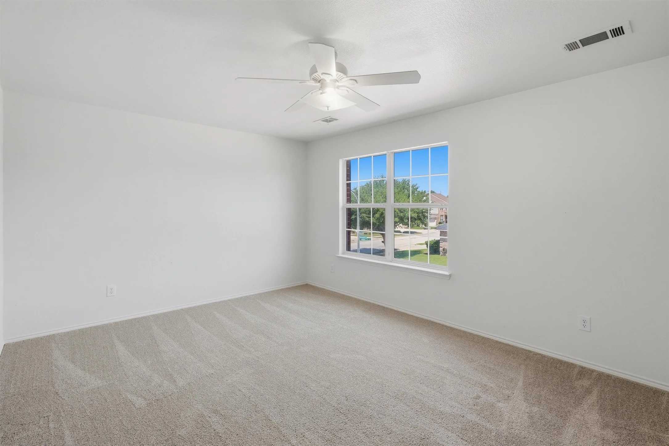 Bright interior with neutral carpeting, white walls, a multi-pane window, and a ceiling fan with integrated lighting