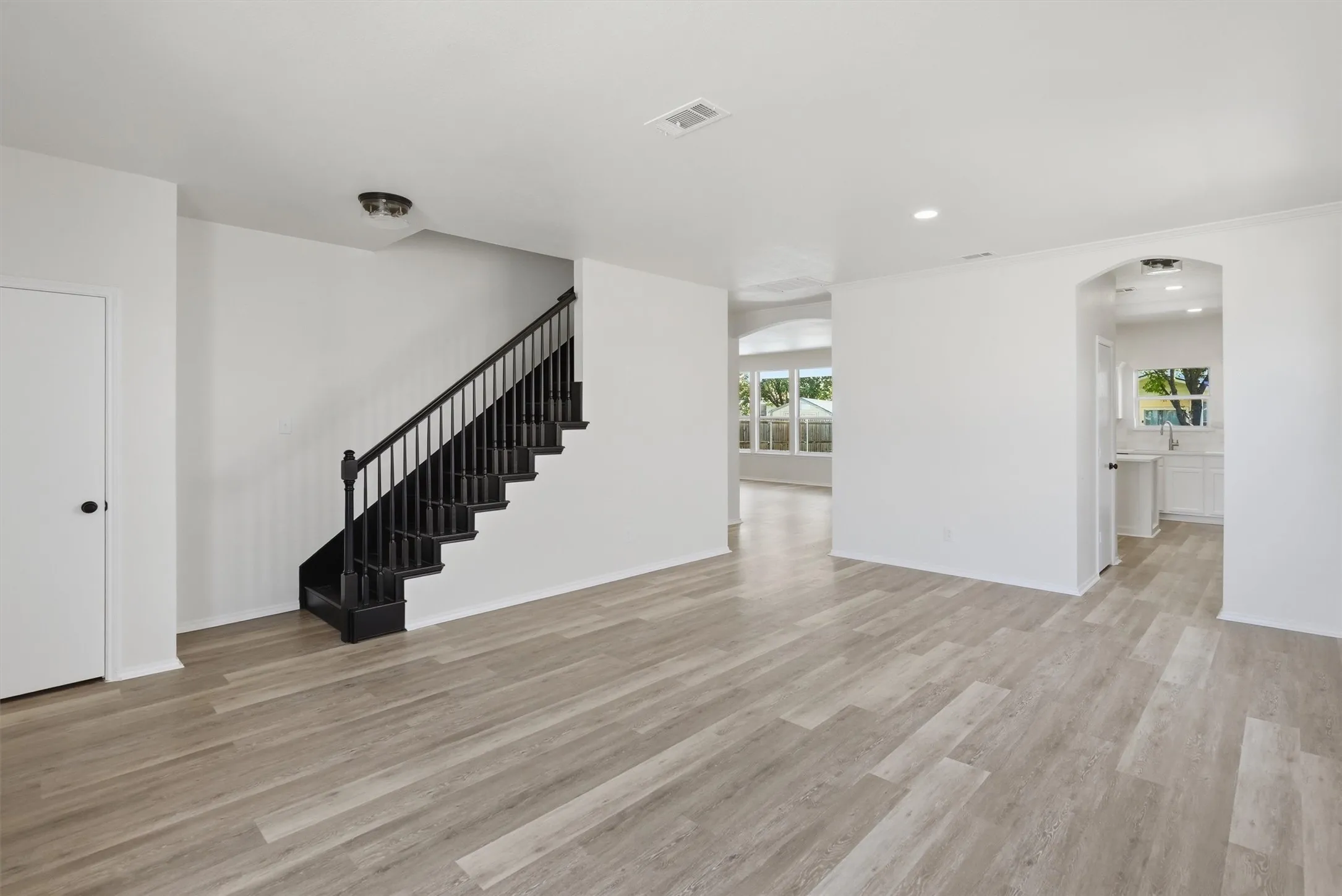 Wood-finish flooring throughout, black staircase with balusters, arched doorway, and white interior walls