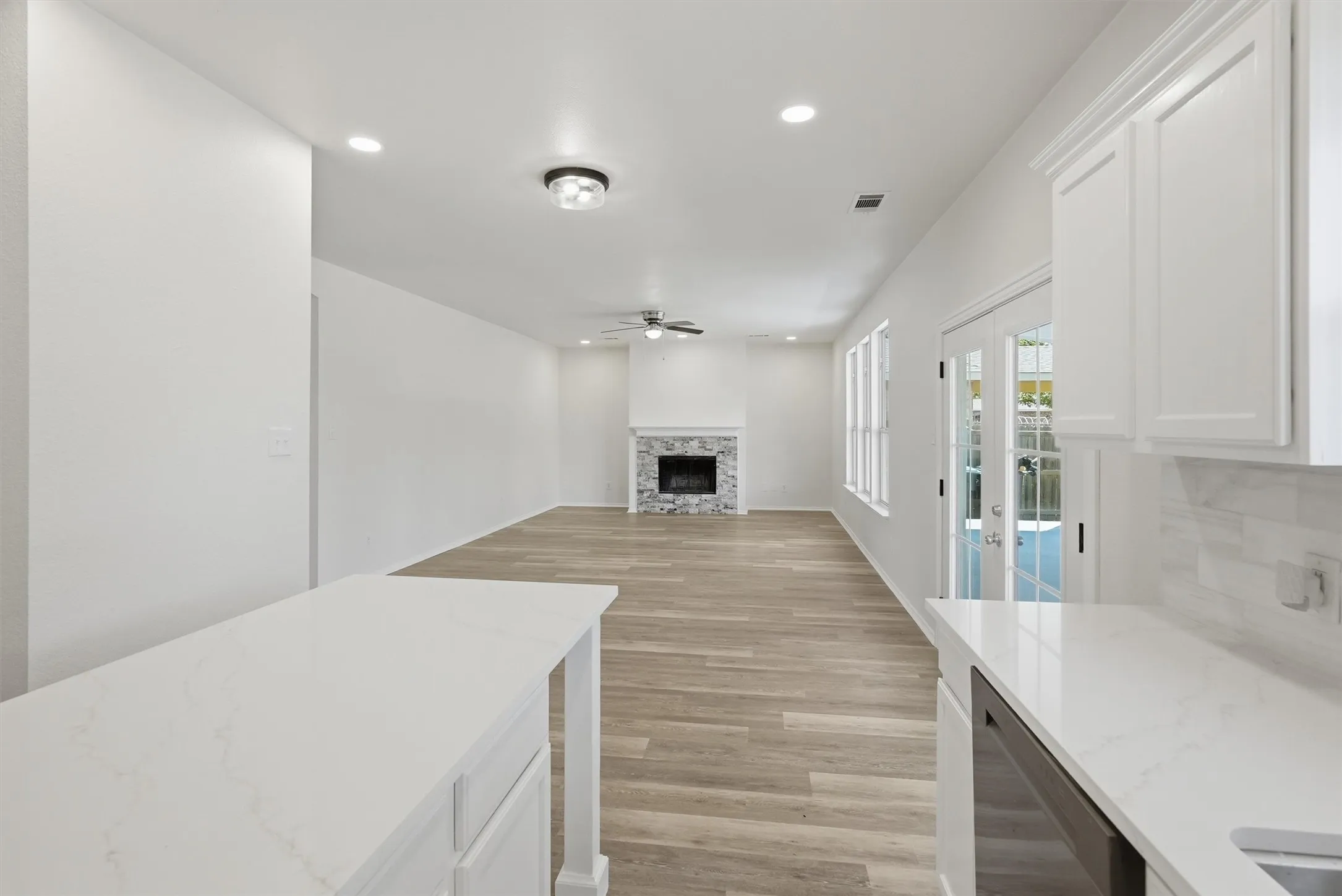 White cabinetry with quartz countertops, a tile backsplash, wood-finish flooring, a stone-faced fireplace, and recessed lighting