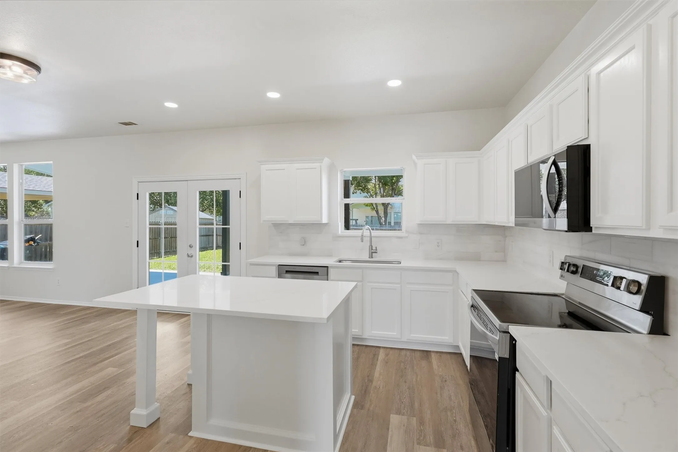 Contemporary kitchen featuring white cabinetry, light-toned countertops, stainless steel appliances, and a central island