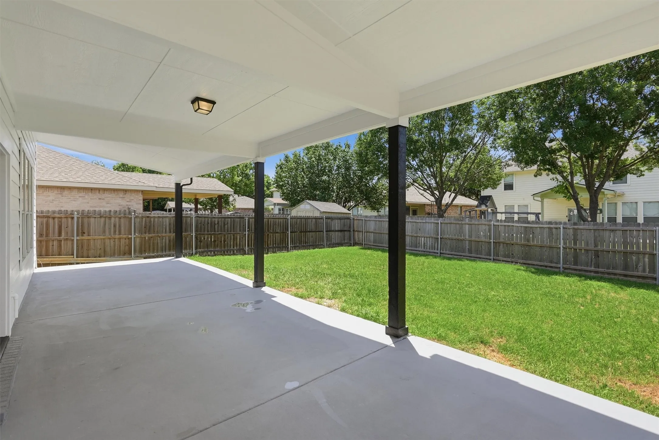 Covered patio with a concrete surface, black support columns, and an overhead light fixture