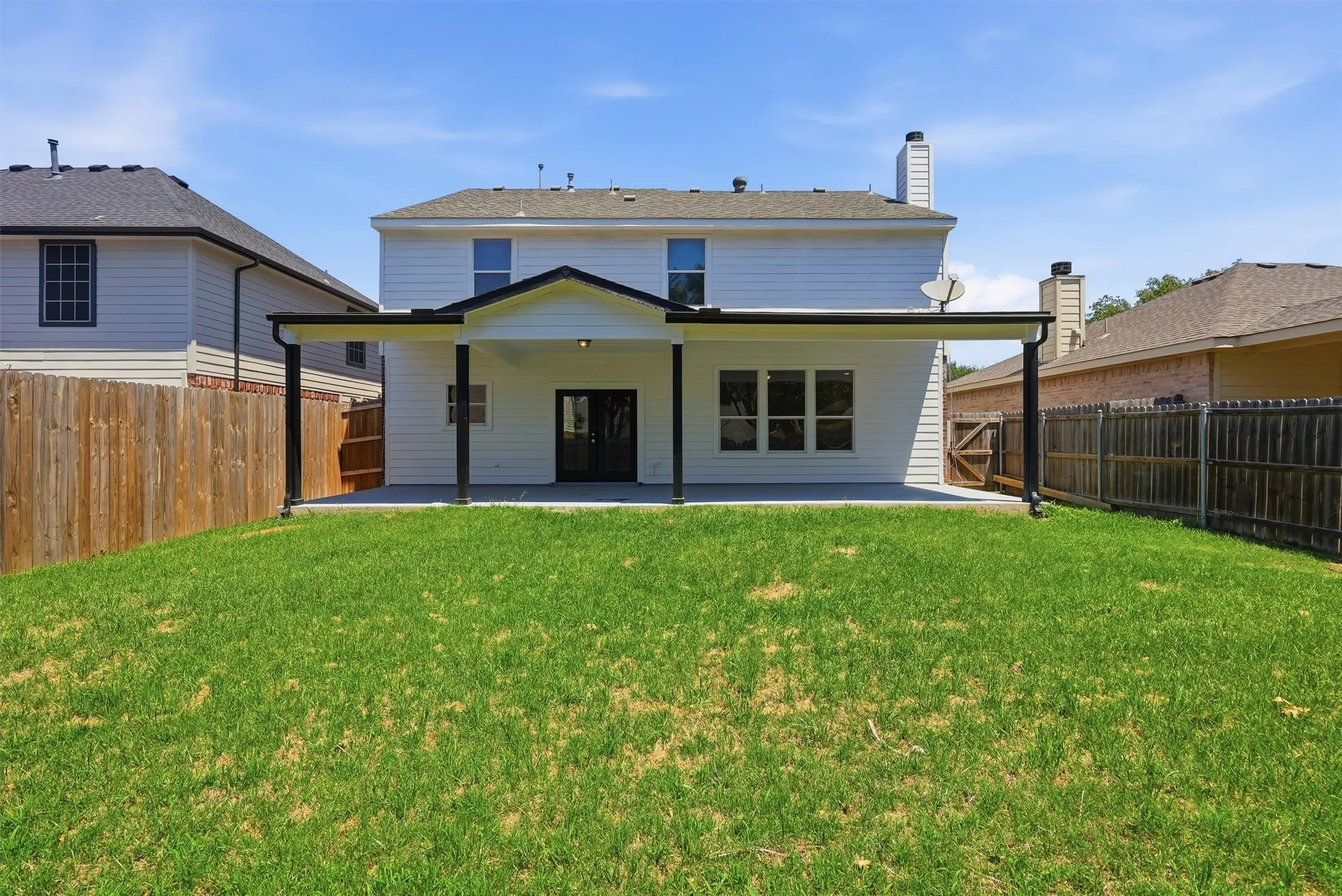 Expansive lawn with a covered concrete patio, white siding, and a fenced perimeter