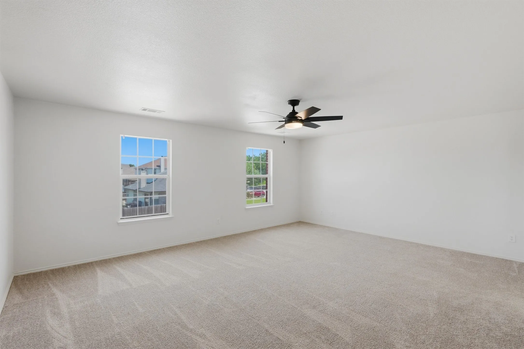 Spacious room featuring neutral carpeting, white walls, two multi-pane windows, and a ceiling fan with integrated lighting