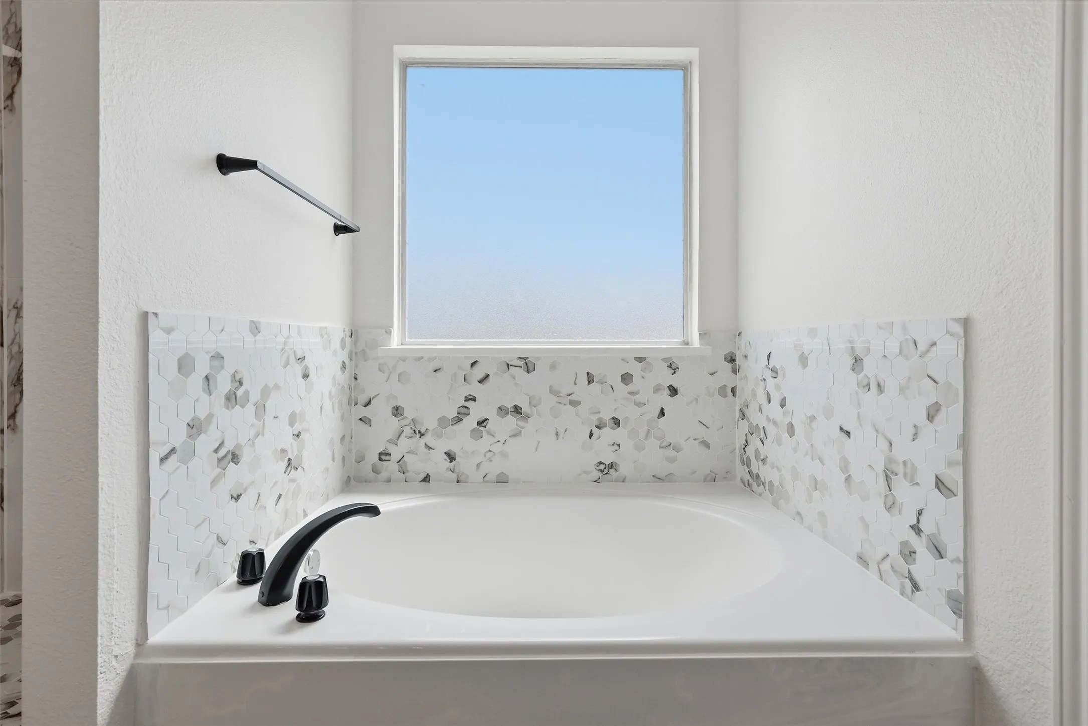 Built-in soaking tub featuring matte black fixtures and a tiled surround with hexagonal mosaic accents
