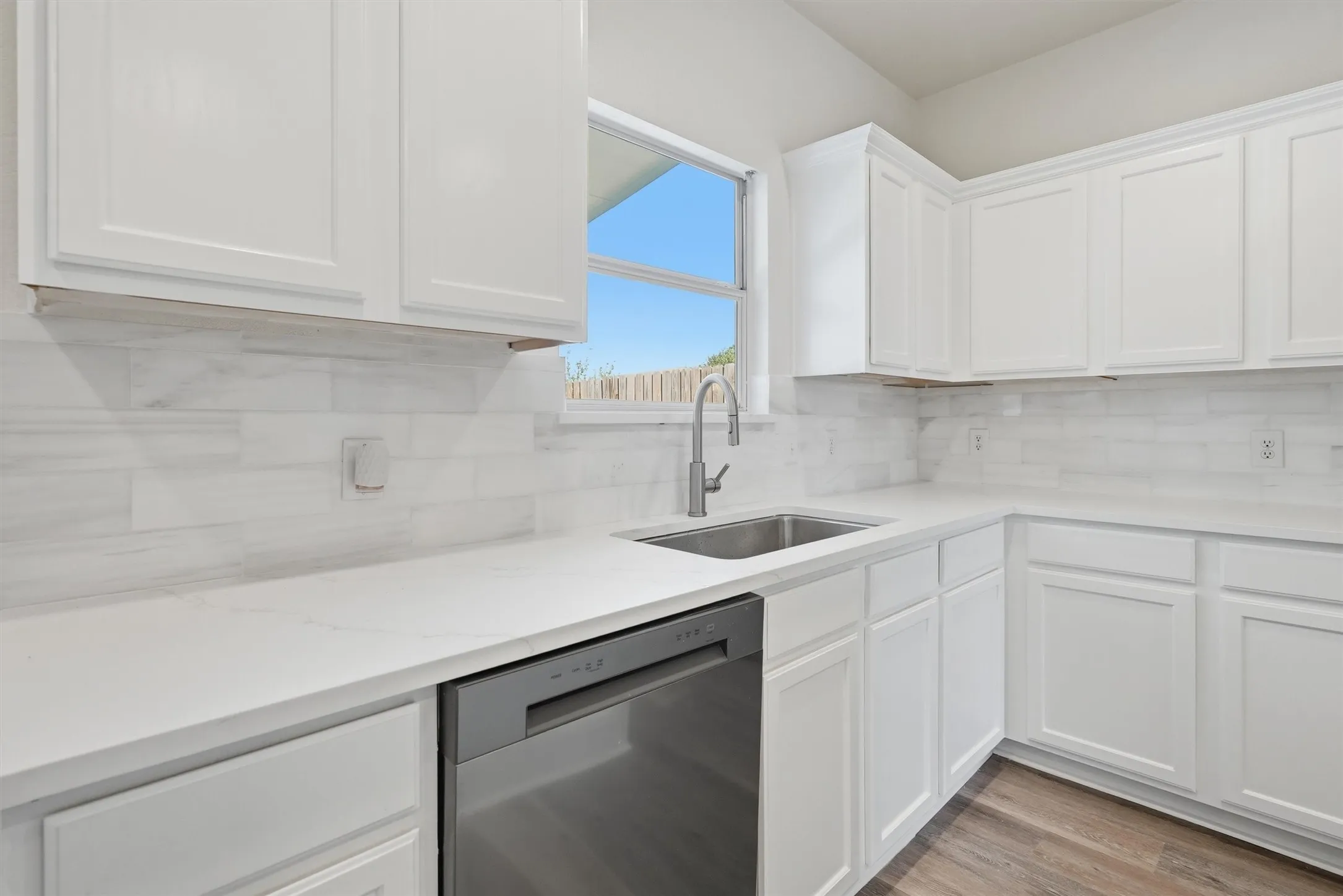 White cabinetry with brushed nickel hardware, stainless steel sink with gooseneck faucet, light-toned countertop, and wood-finish flooring