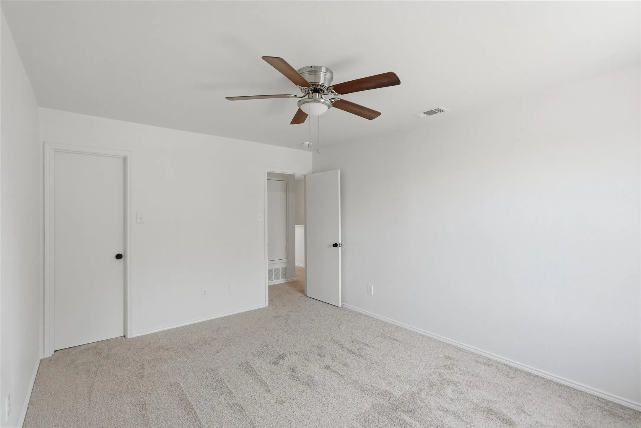 Neutral tone wall finishes, light gray carpeting, and a ceiling fan with wood-finish blades