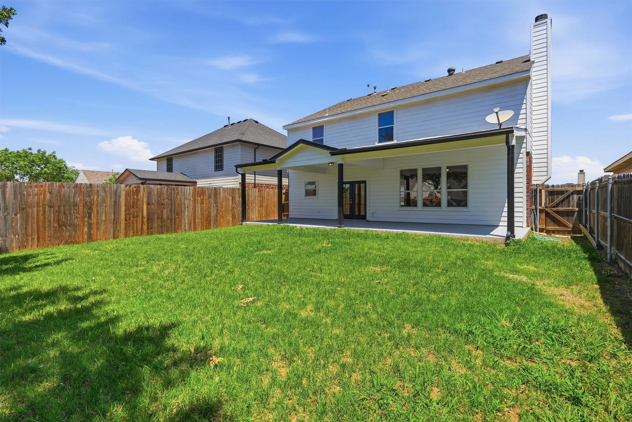 Expansive grassy yard with wood fencing, a covered patio, and a two-story exterior