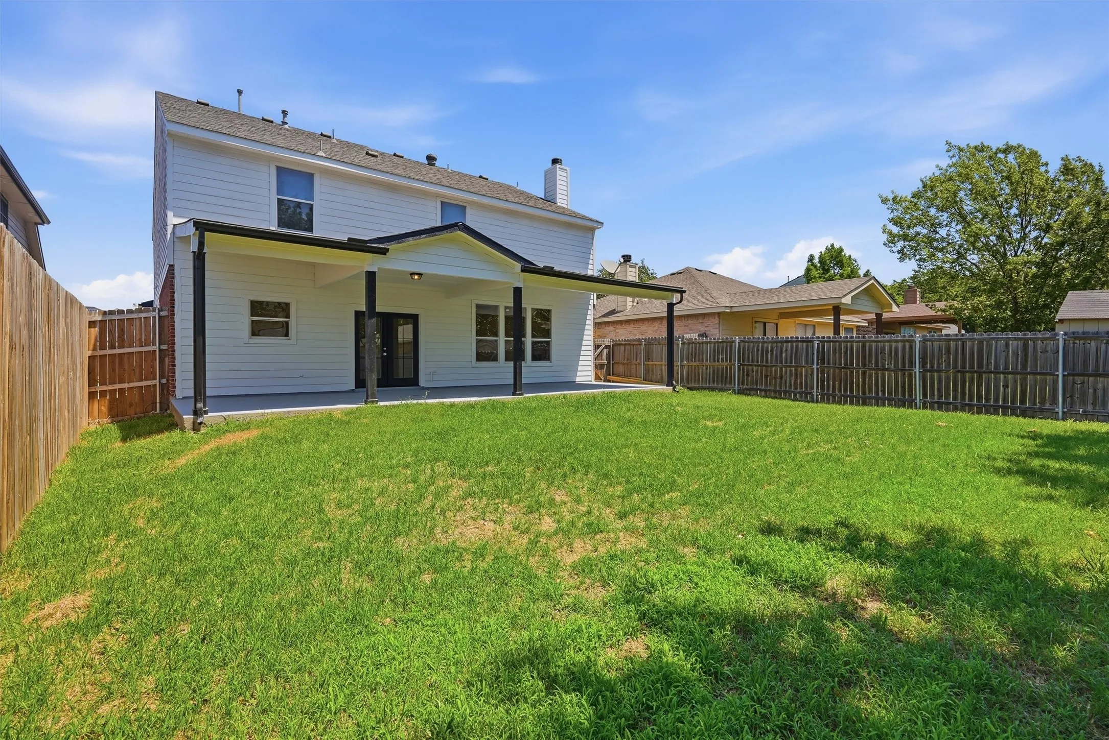 Expansive grass lawn with a covered patio featuring a black-framed door and windows