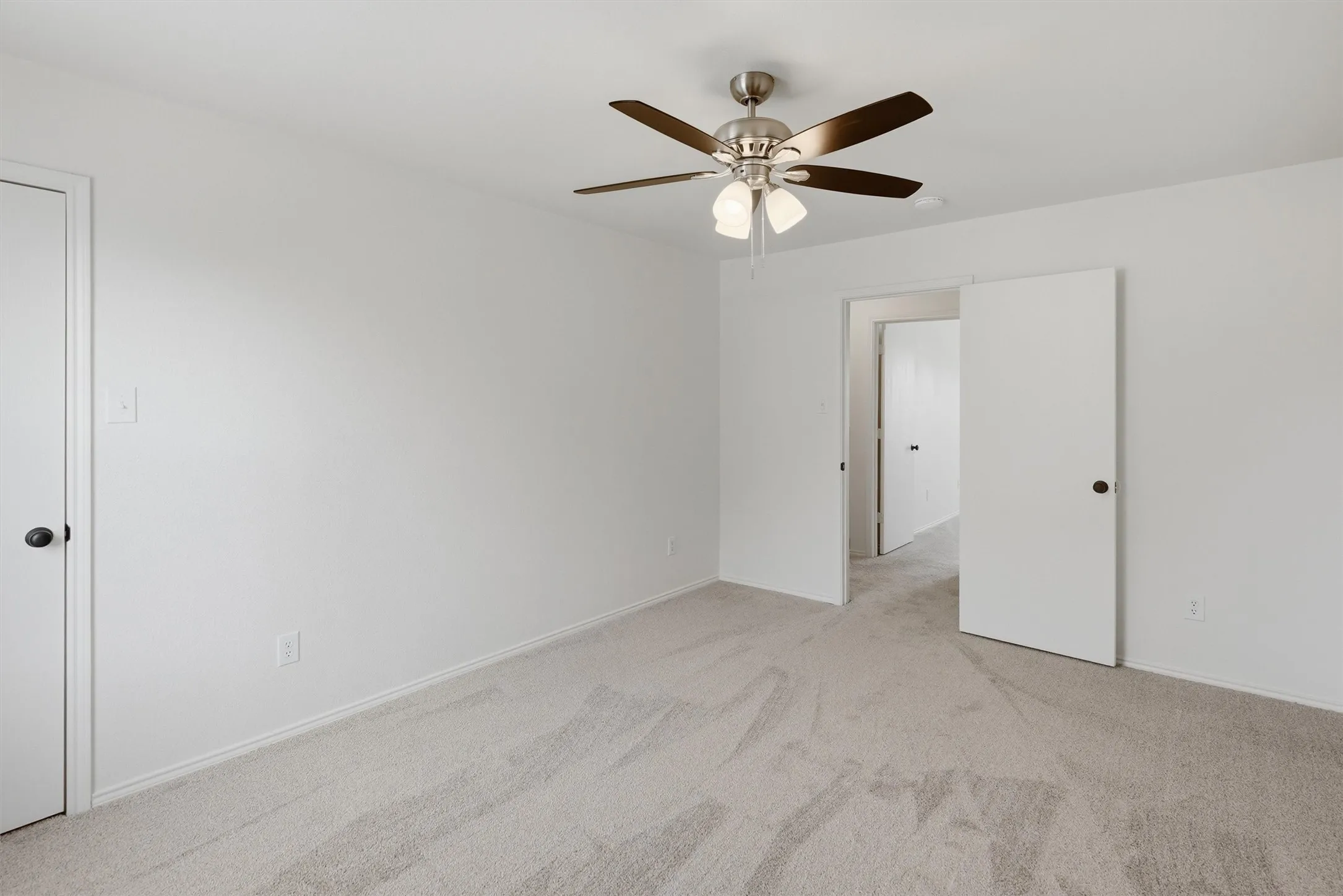 Neutral tone wall paint, light-colored carpeting, brushed nickel ceiling fan with light fixture, white interior doors