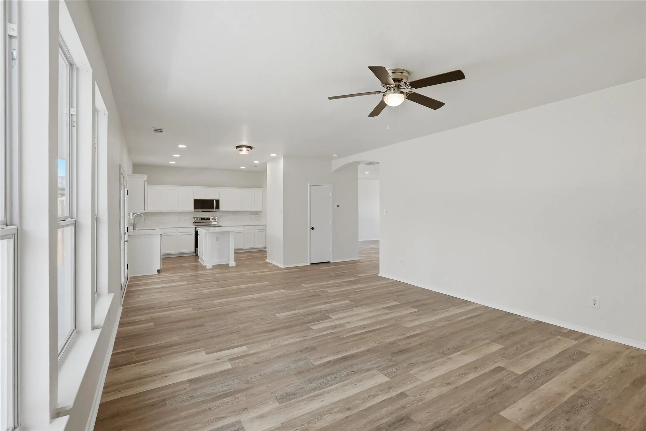 Expansive open concept living area featuring wood-finish flooring, ceiling fan with integrated lighting, and multiple windows