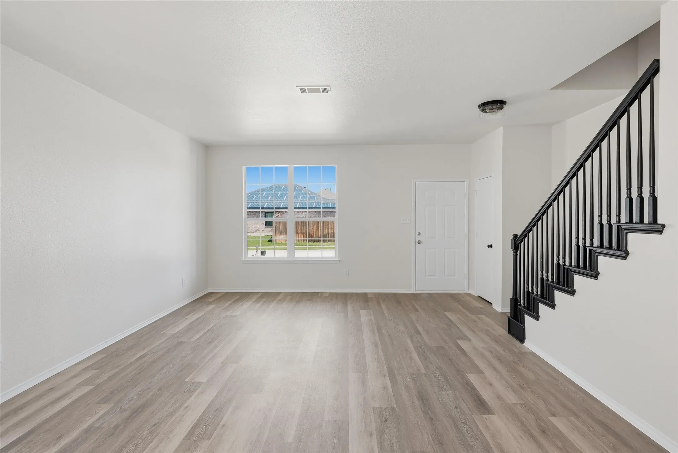 Spacious room featuring wood-finish flooring, a multi-pane window, and a prominent staircase with dark balusters