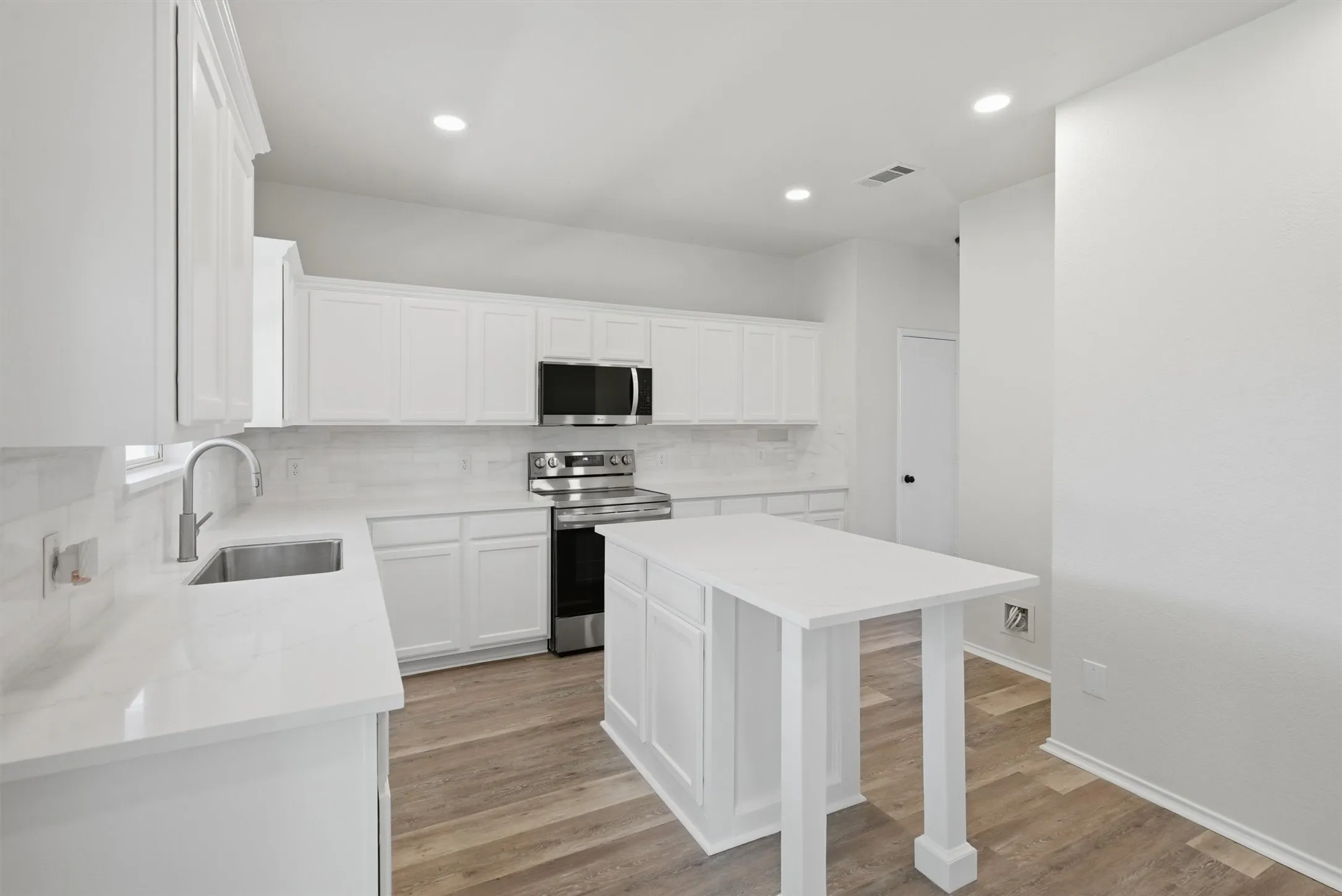 Bright kitchen featuring white cabinetry, light countertops, wood-finish flooring, stainless steel appliances, and an island with counter seating
