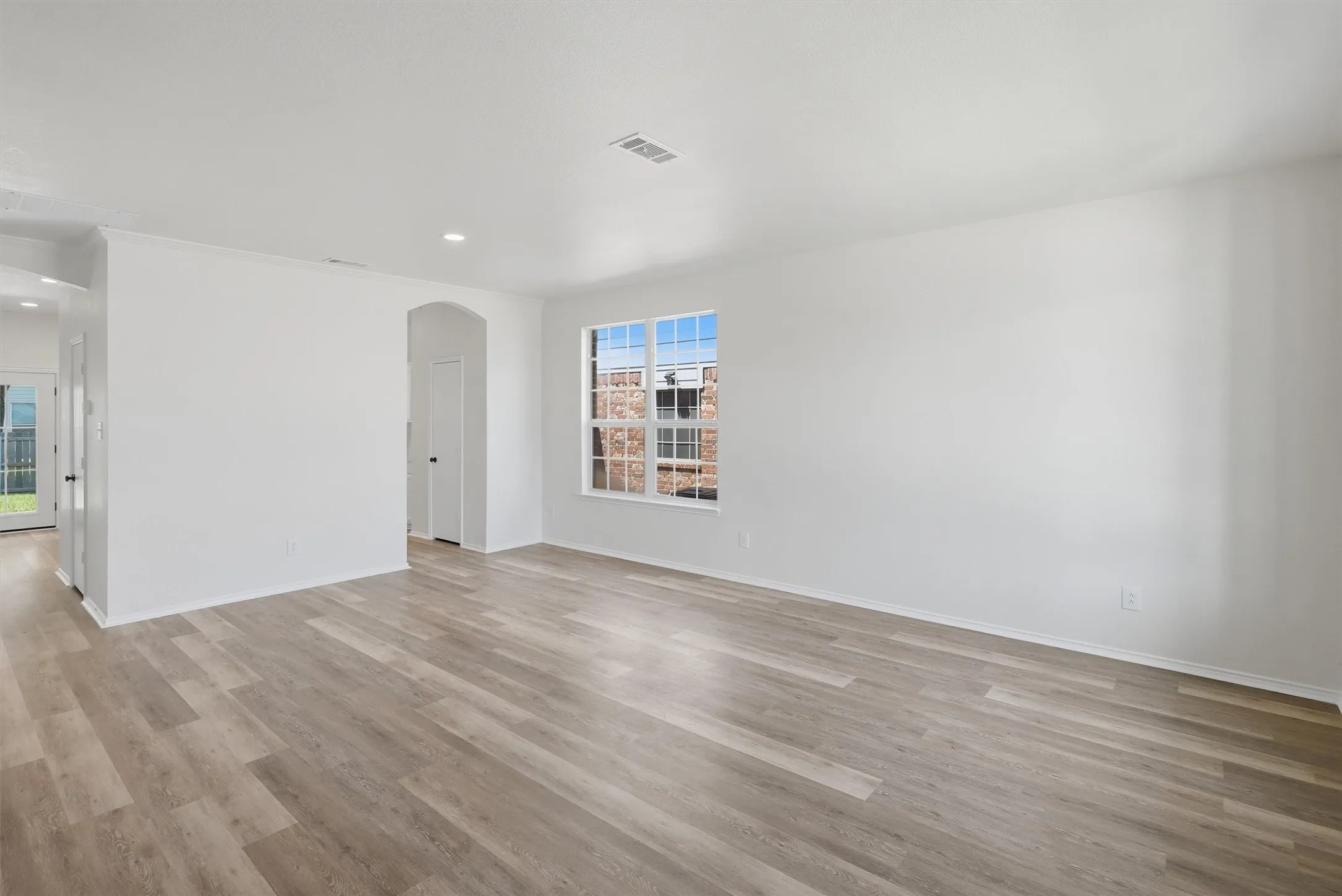 Spacious room with wood-finish flooring, white walls, and a large window with grid panes