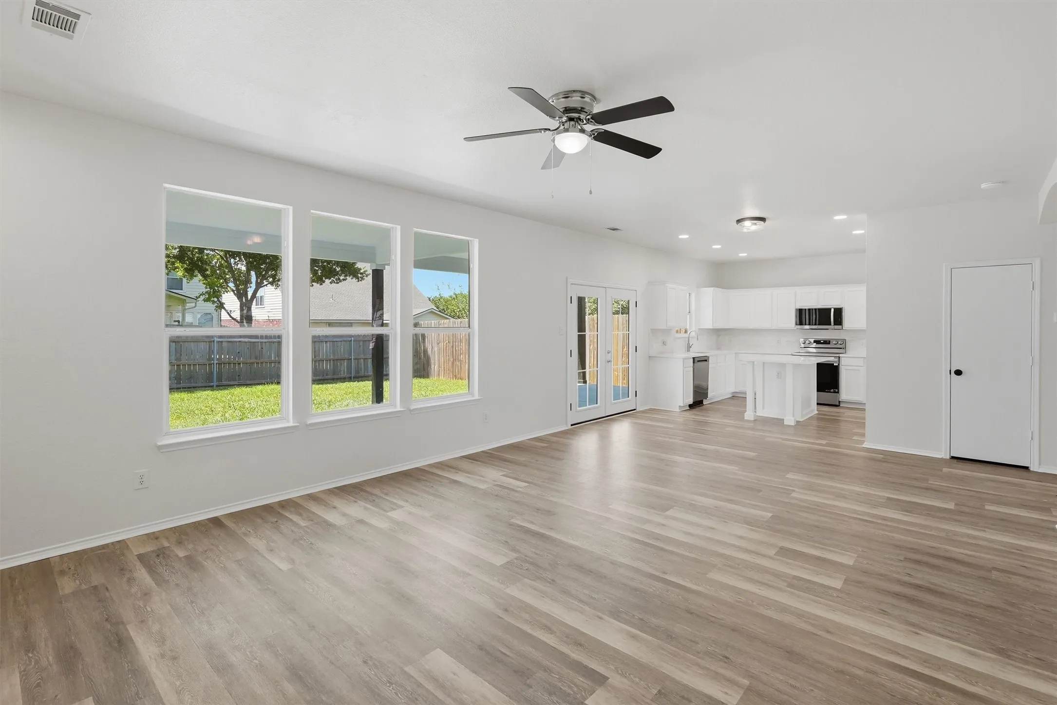 Spacious living area featuring wood-finish flooring, a ceiling fan, and multiple windows