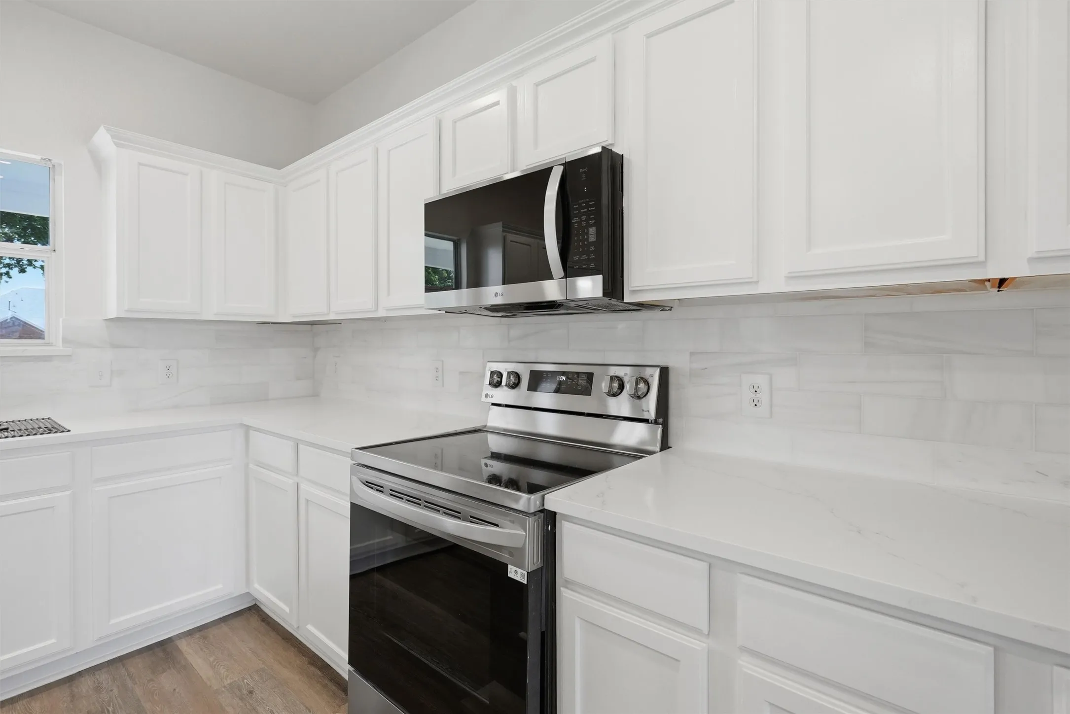 White shaker-style cabinetry, stainless steel range, built-in microwave, white countertops, and subway tile backsplash