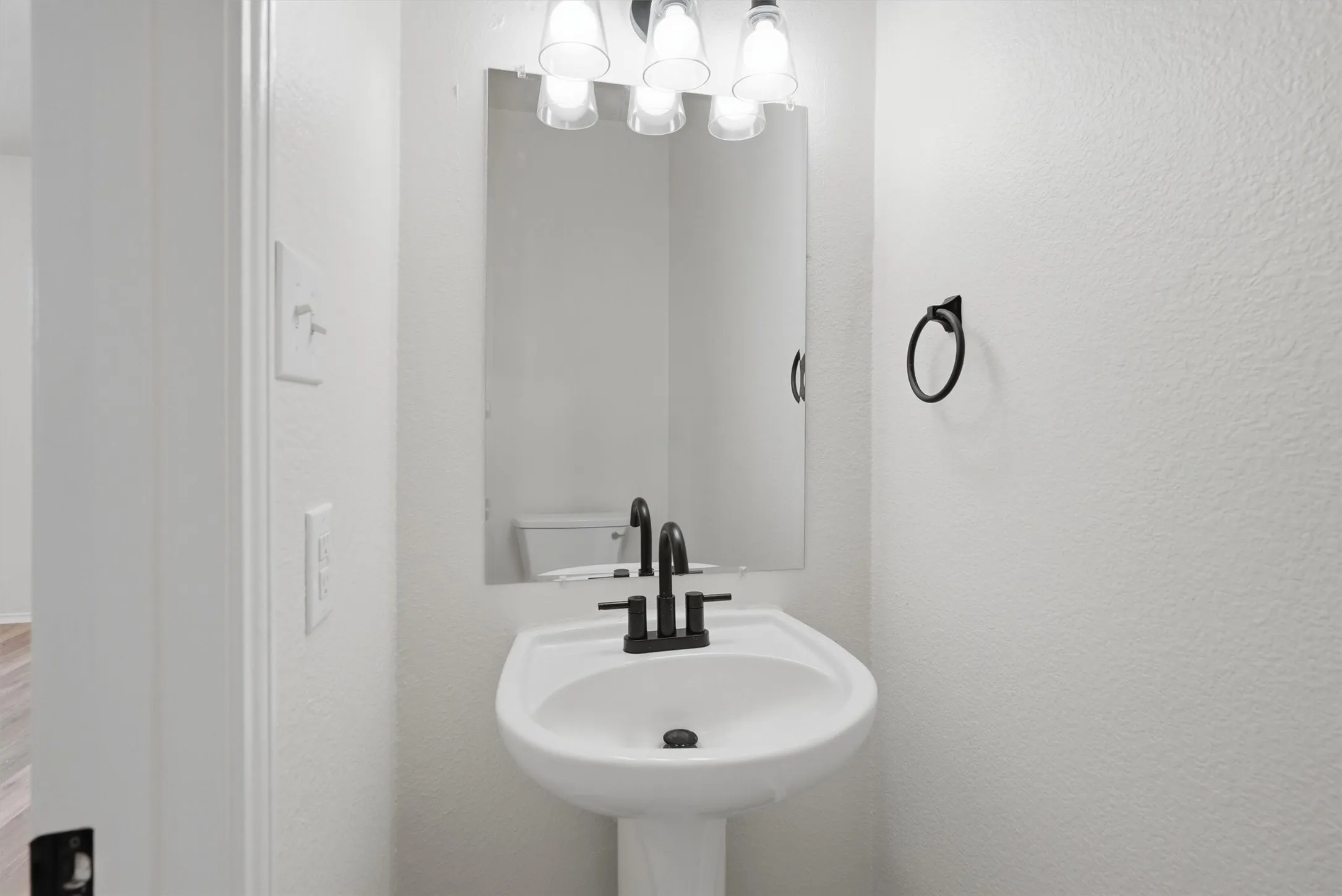 White pedestal sink with black fixtures and a wall-mounted mirror