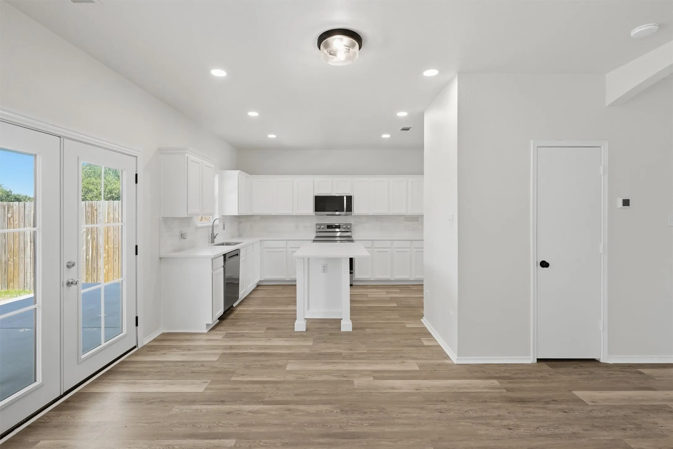 Kitchen featuring an island, white cabinetry, integrated stainless steel appliances, and wood-finish flooring
